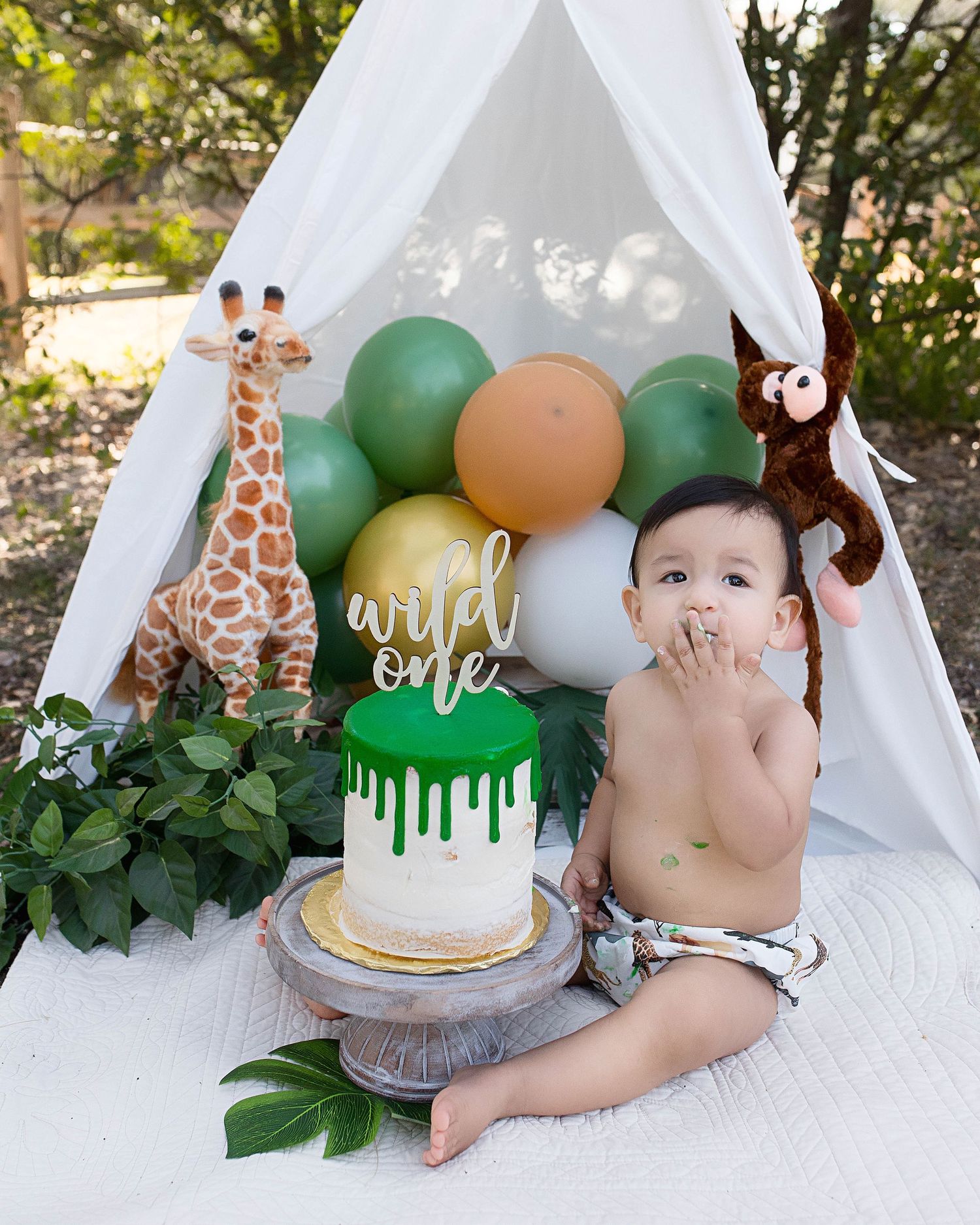 Safari themed first birthday setup with white tent, green balloons and birthday cake.