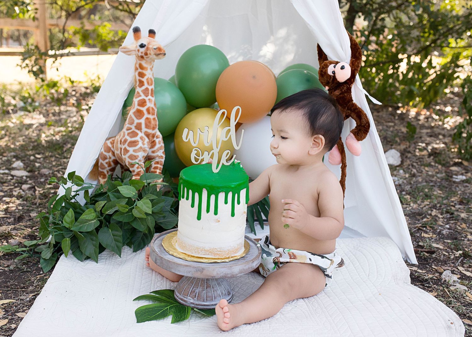 Wild one birthday setup featuring white tent, giraffe toy and green drip cake.
