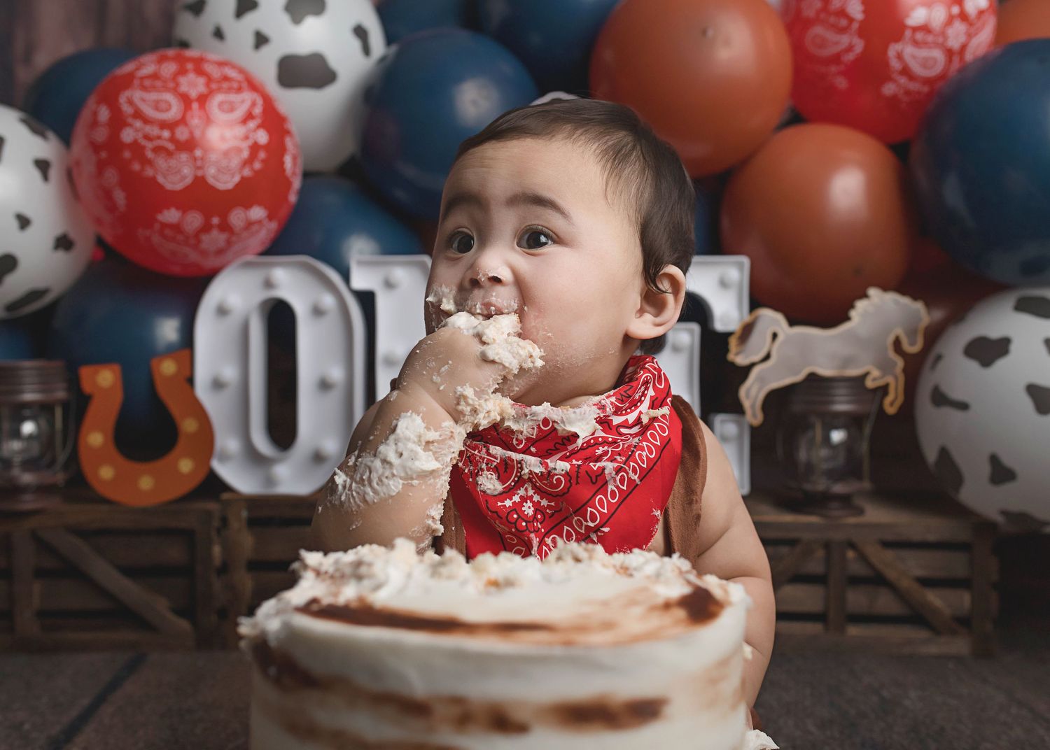 Baby enjoying cake smash session with frosting on face during first birthday photoshoot.