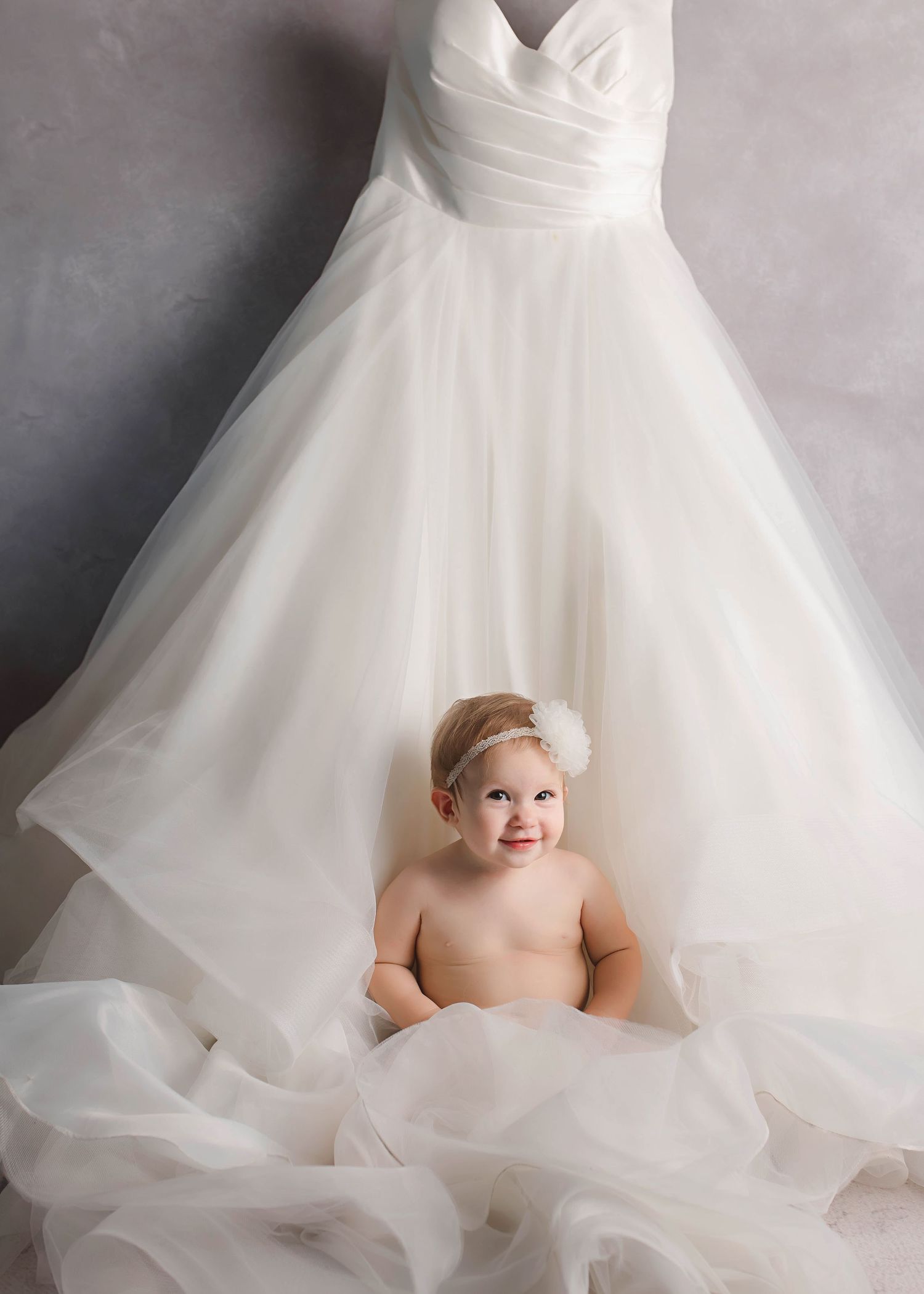 Baby portrait session with flowing white wedding dress as elegant backdrop.