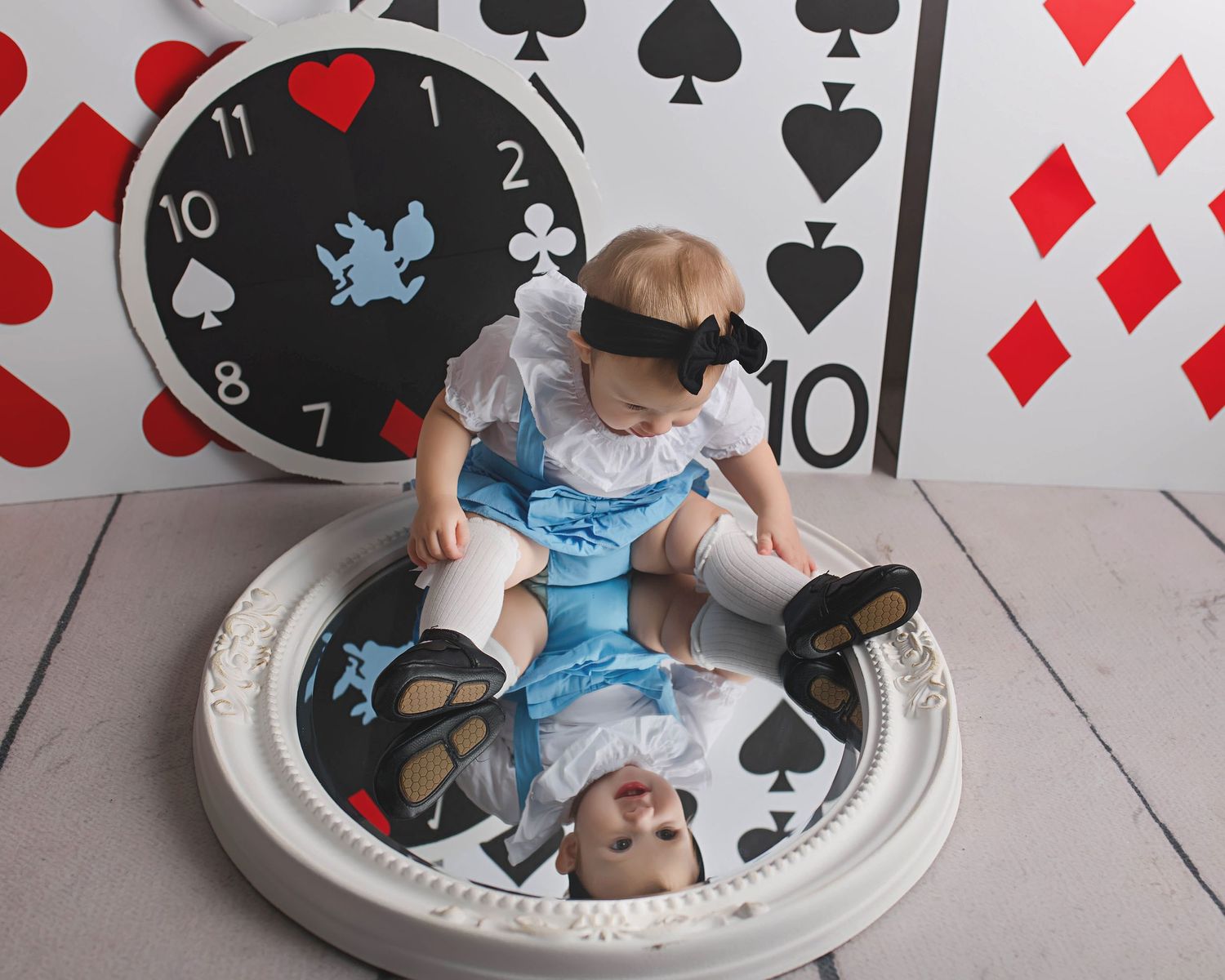 Alice in Wonderland themed photo setup with playing cards and clock backdrop.