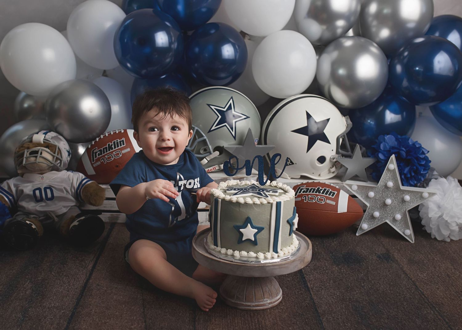 Baby boy celebrating first birthday with Cowboys themed cake and balloon decorations.