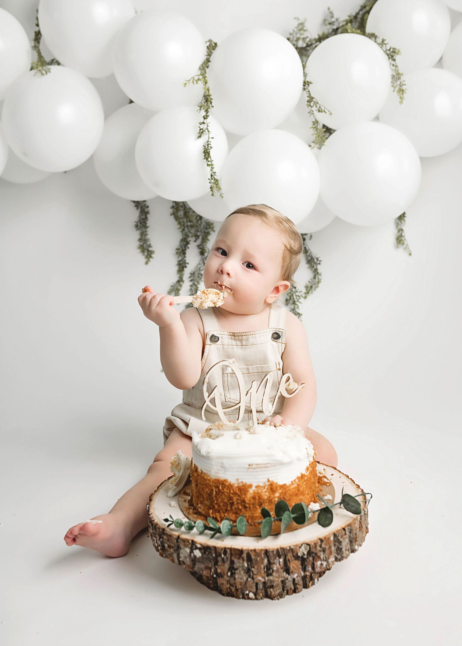 Cake smash photography setup with rustic cake stand and white balloon backdrop.