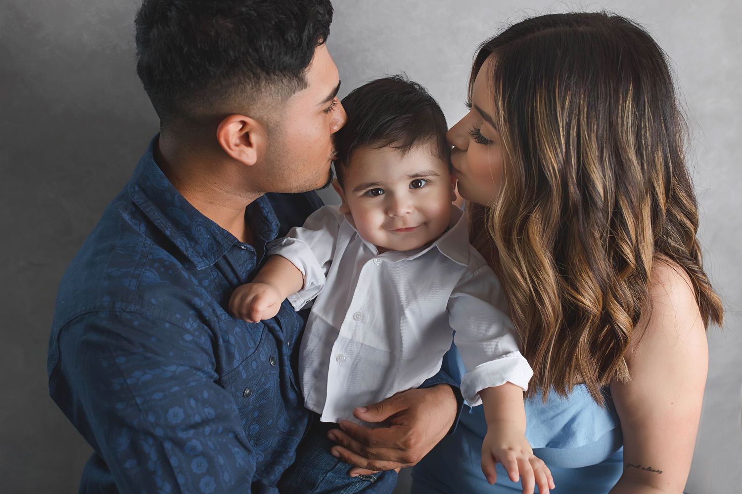 An intimate family portrait in muted tones against gray backdrop.