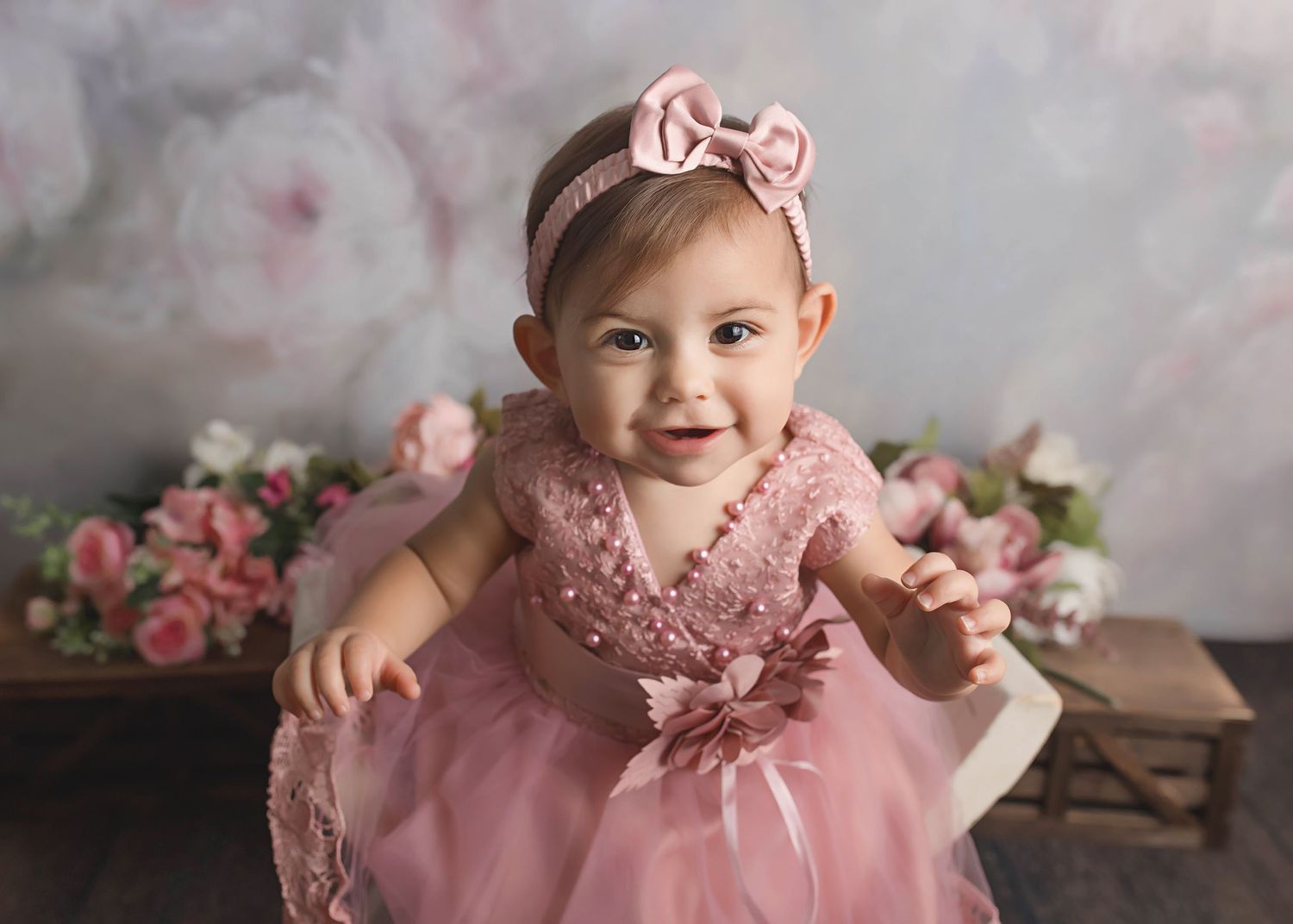 Sweet portrait of a baby in a pink tulle dress with bow against floral backdrop.