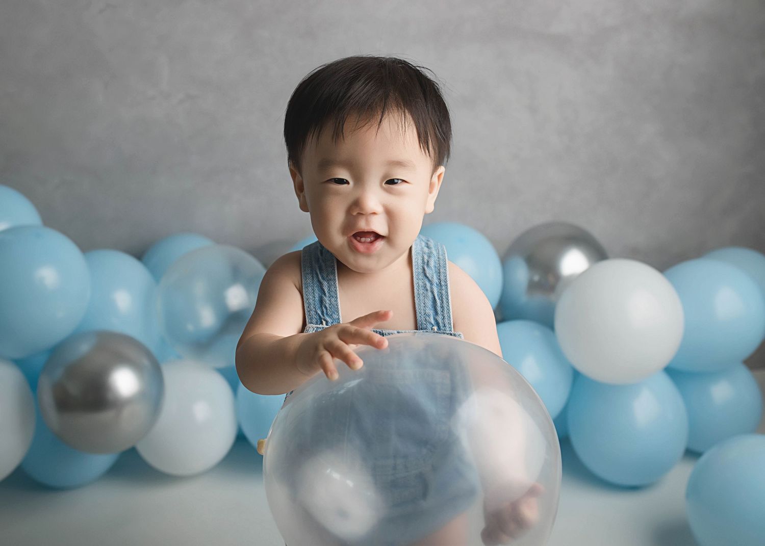 Smiling baby in denim outfit with silver and blue balloon decorations.