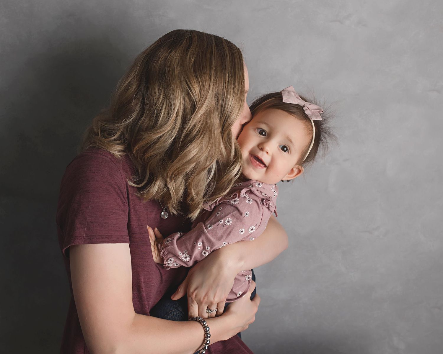 Tender moment captured in studio with muted gray backdrop.