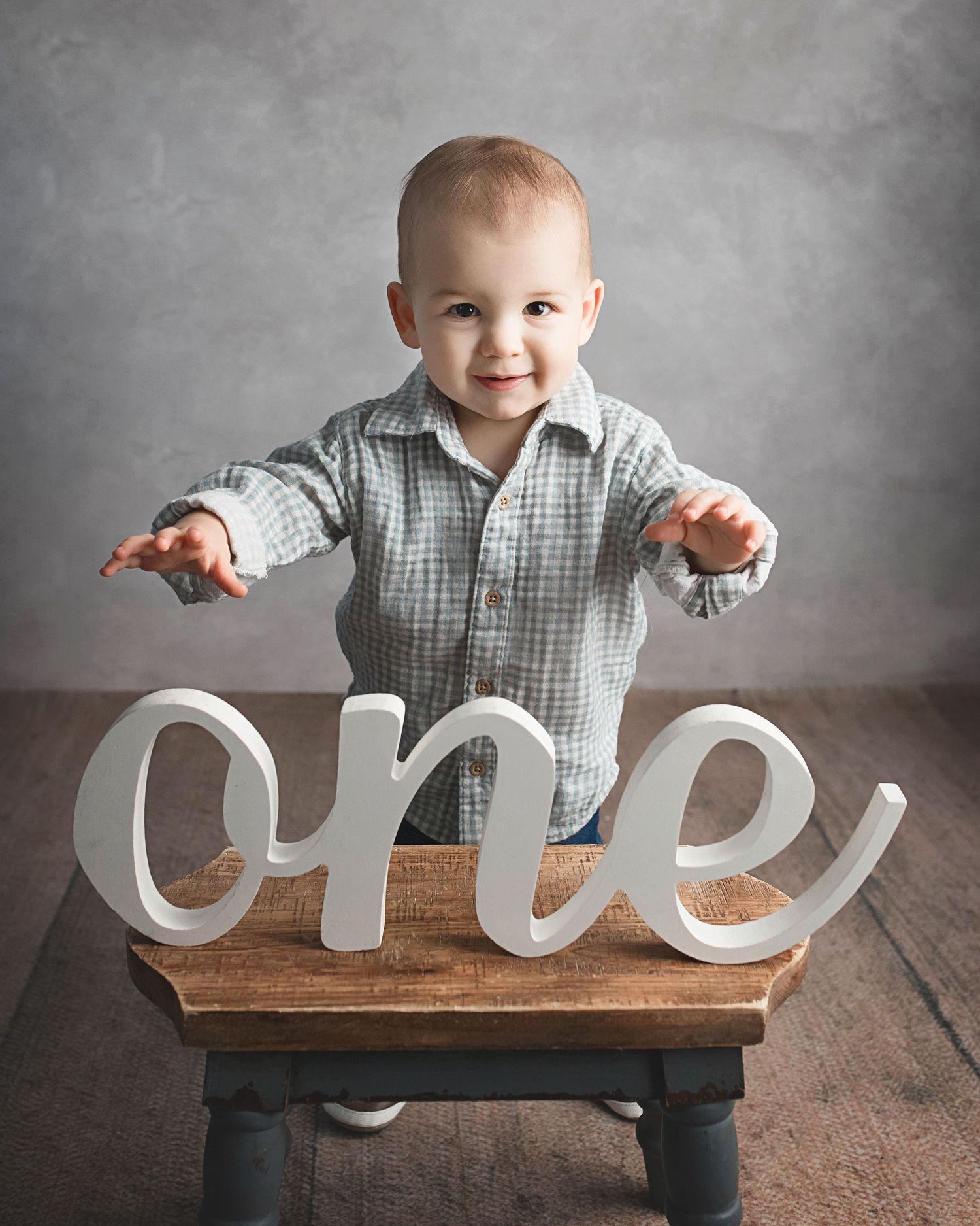 Small child in gray plaid shirt poses with large white 'one' text decoration.