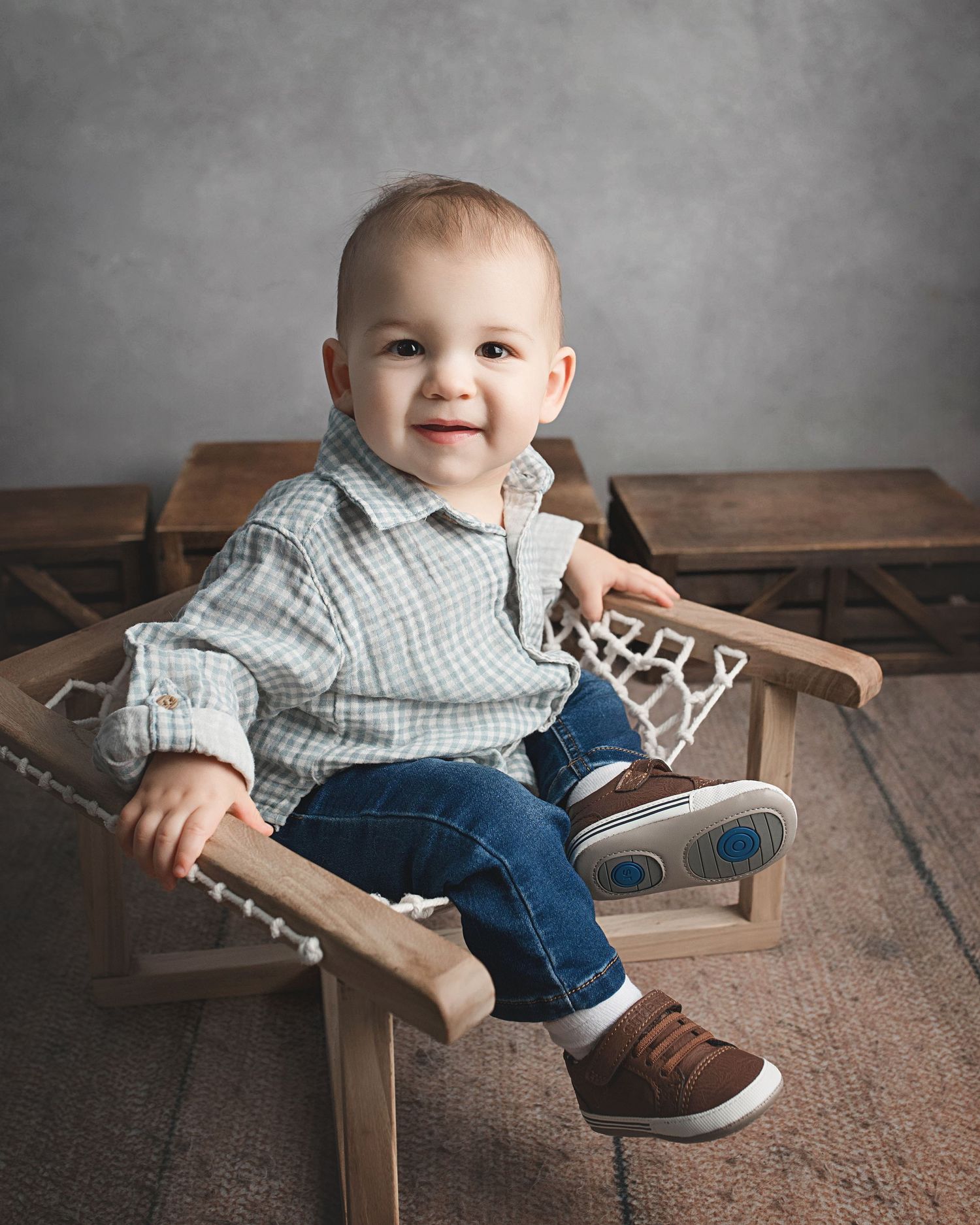 Happy child in checkered shirt sits on wooden chair during portrait session.