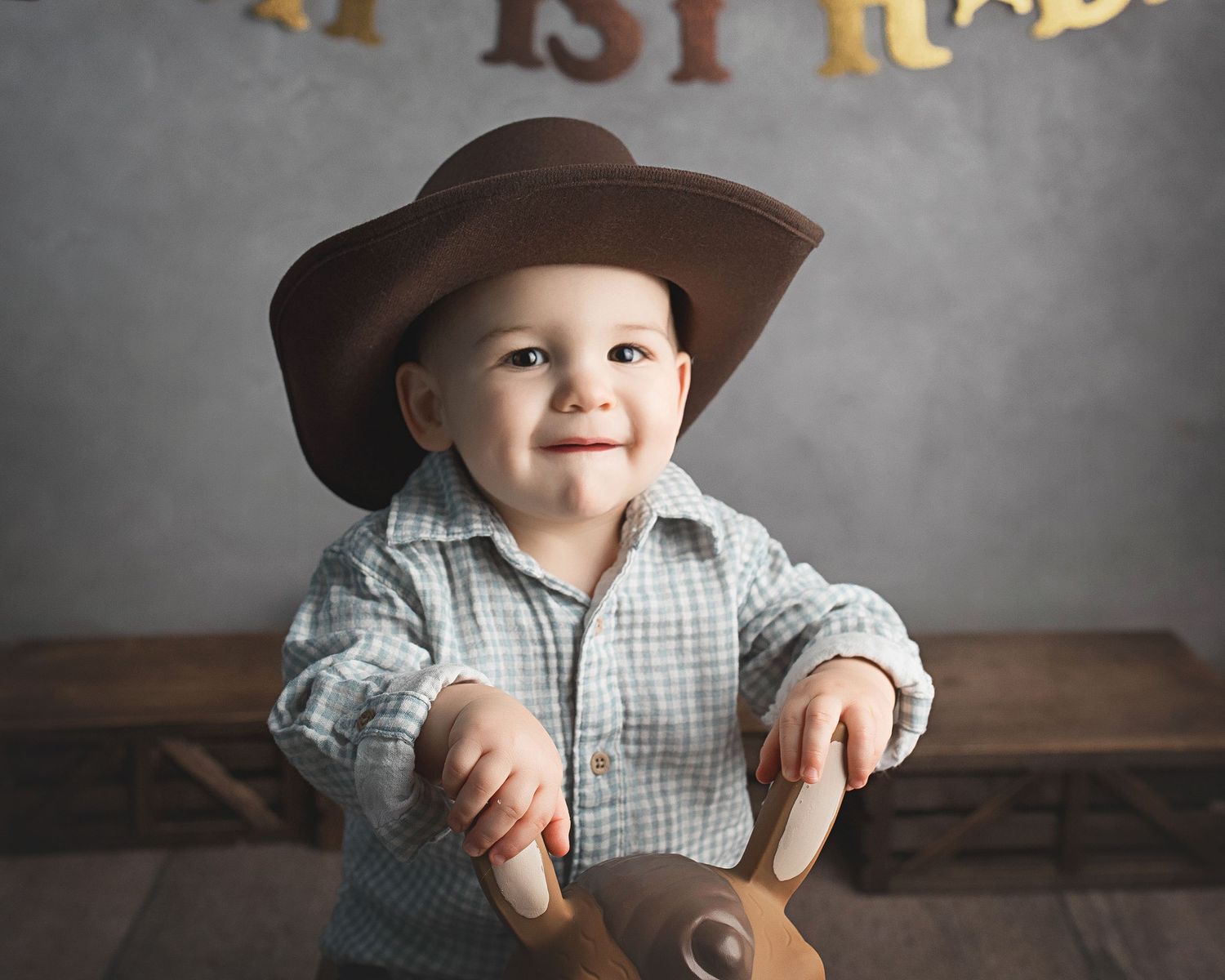 Small child in cowboy hat and plaid shirt poses during photo session.