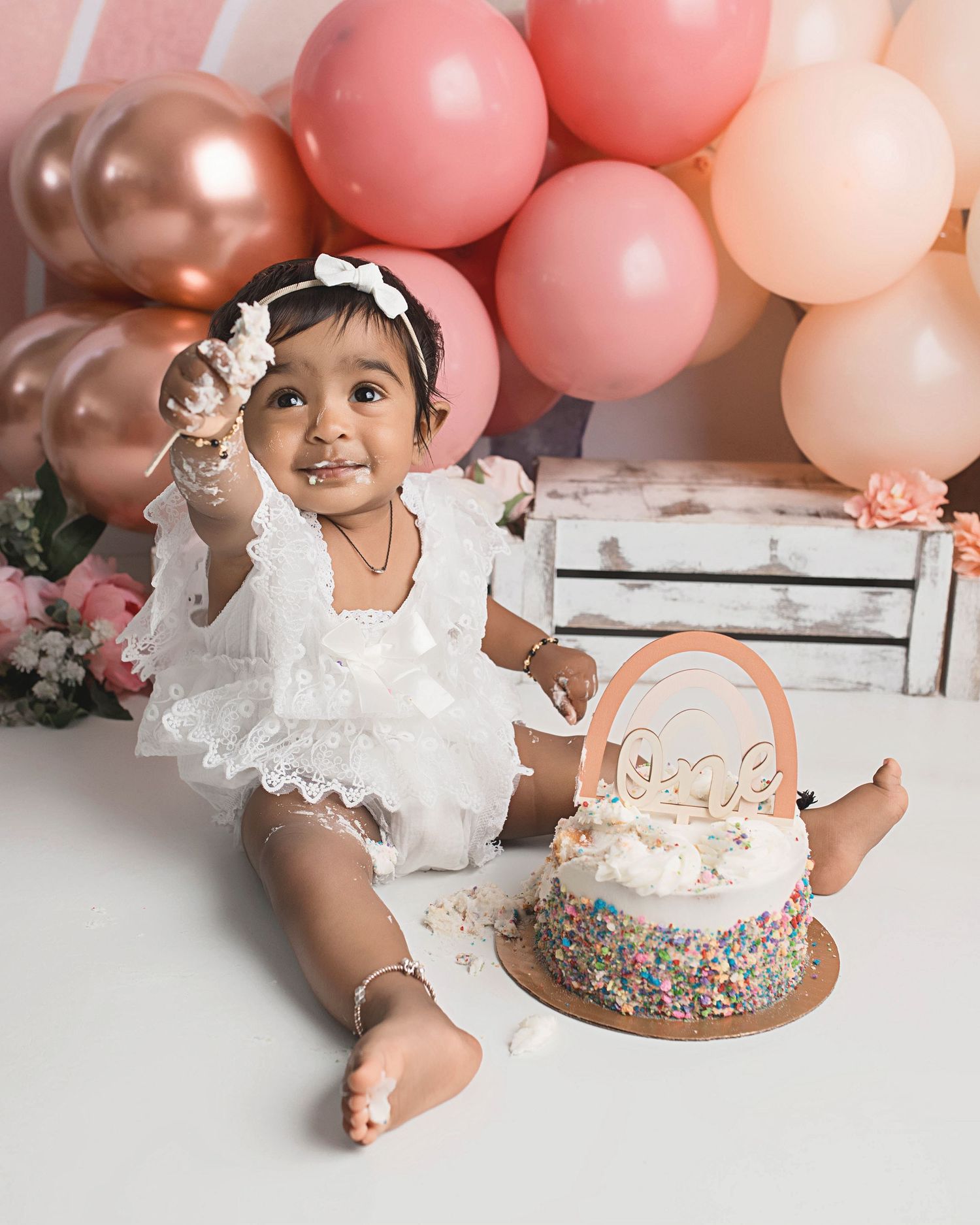 Pink and rose gold balloon arch first birthday setup with sparkly cake.