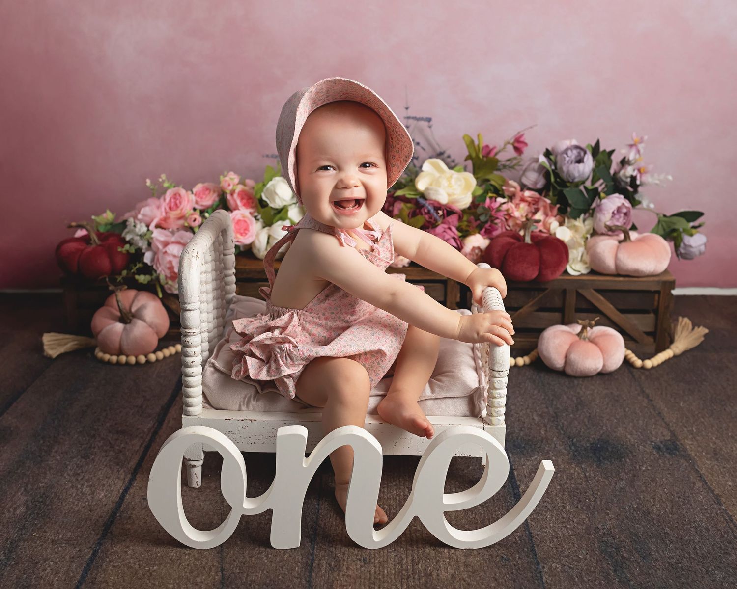 First birthday photo with pink decor, flowers and white 'one' sign.