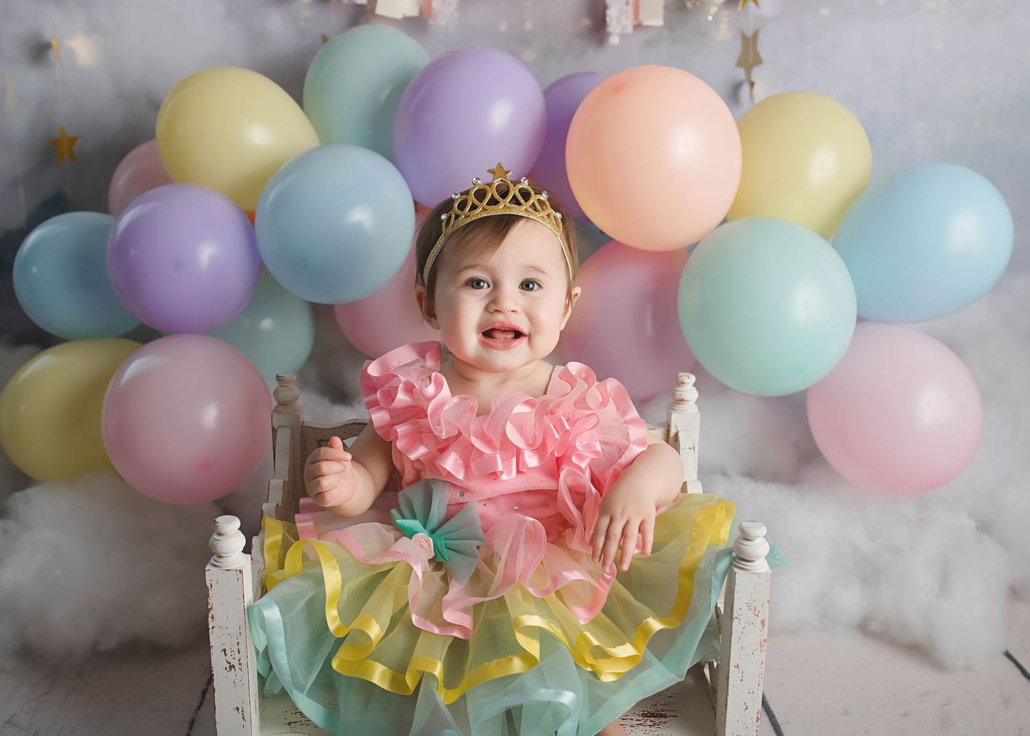 Toddler in pink tutu dress celebrating with balloons and birthday crown.