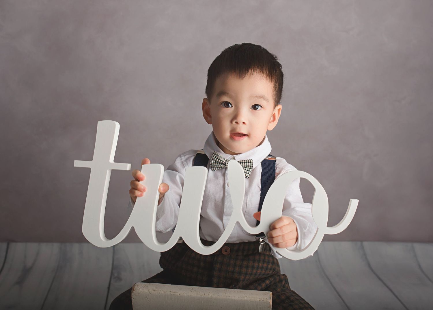 Simple studio portrait with 'two' text prop against grey backdrop.