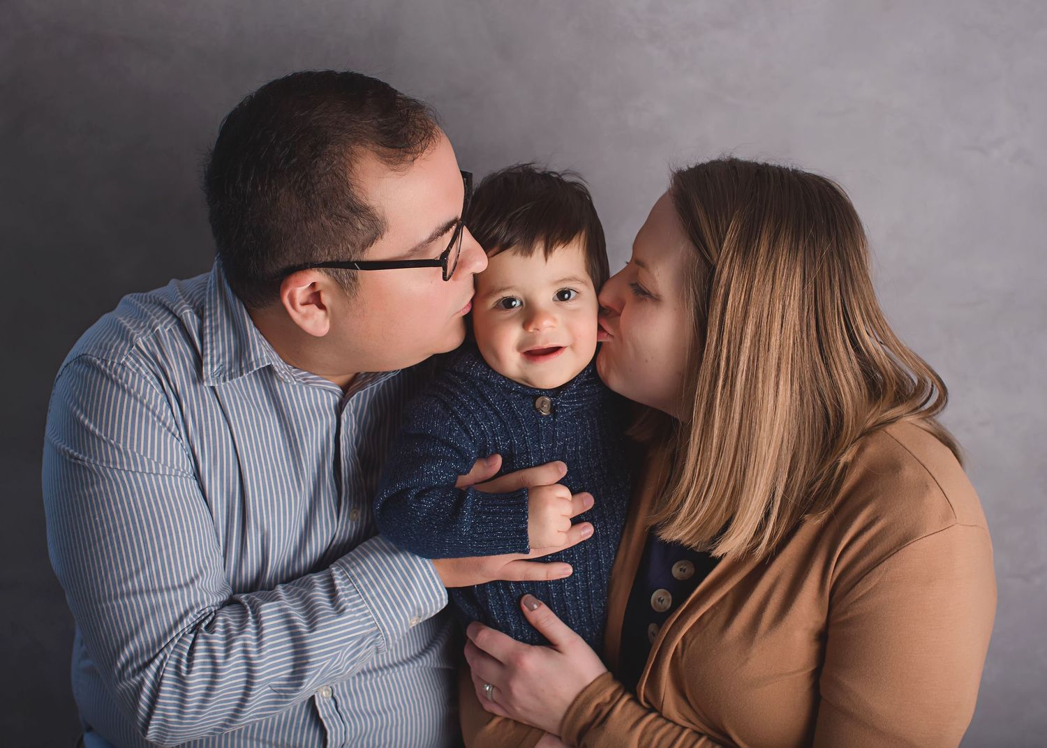 A sweet family moment captured with parents kissing their young child during a professional photography session.