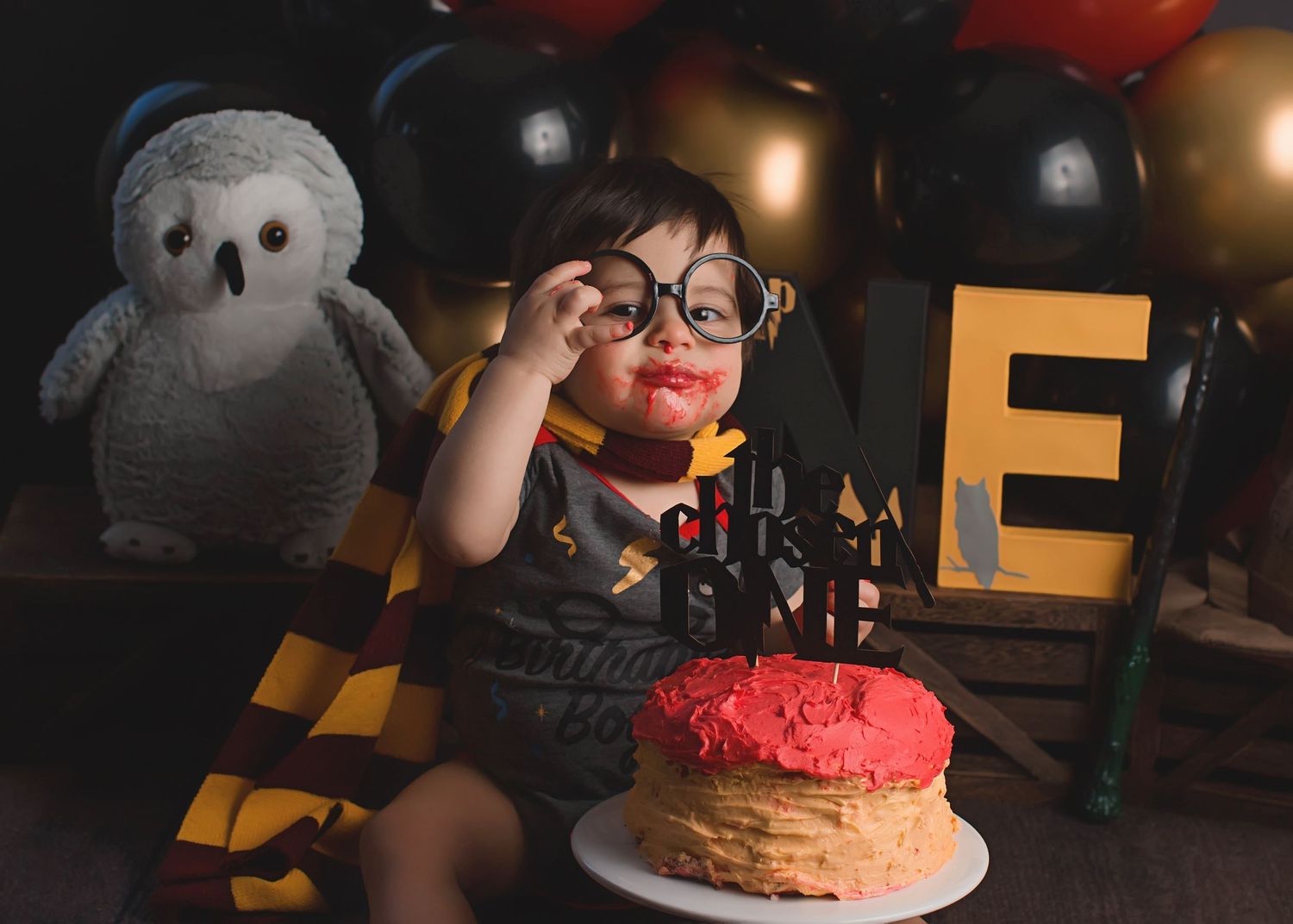 Birthday celebration with cake and stuffed owl against black and gold balloons.