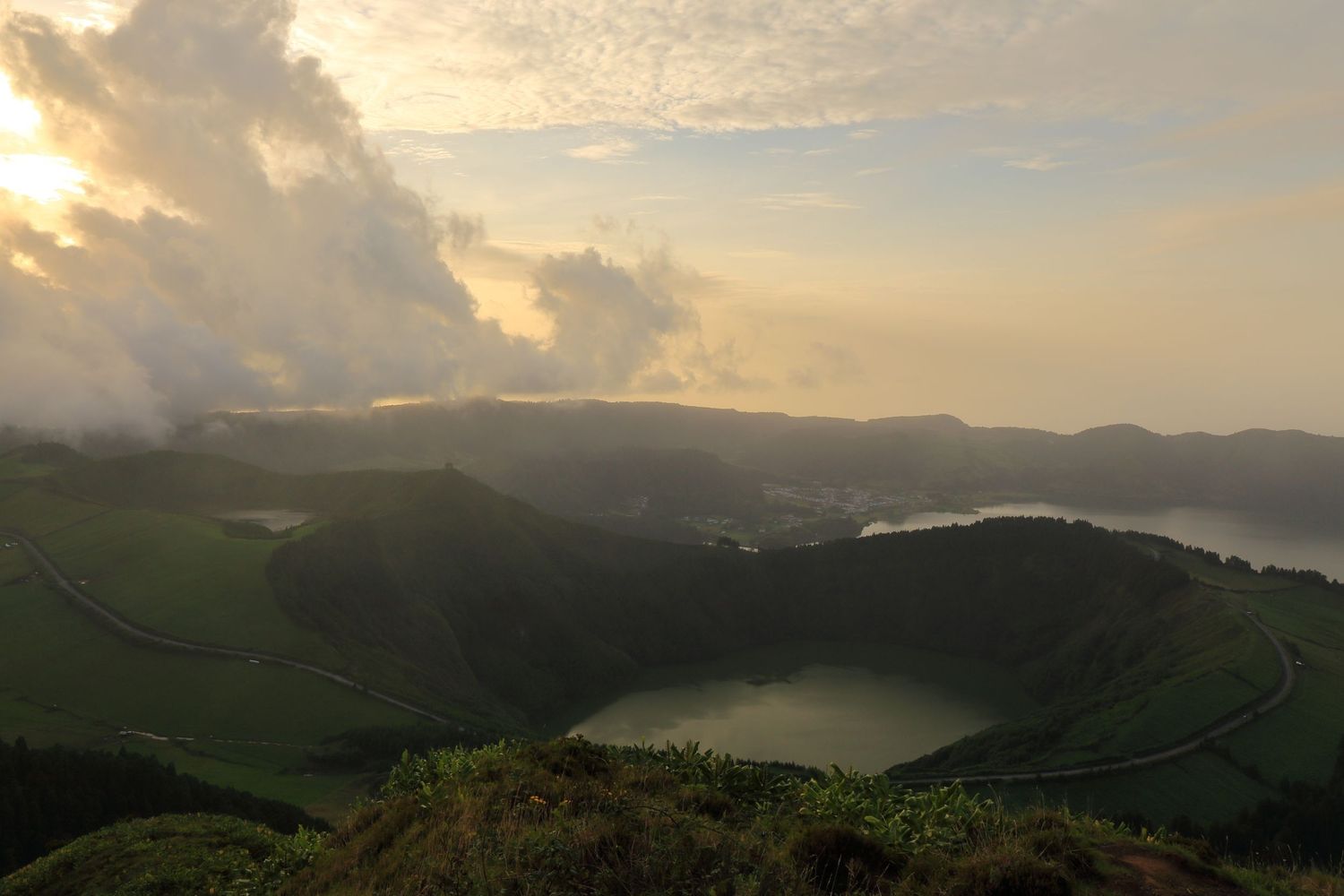 Panoramic view of volcanic lakes nestled between green mountains during sunset.