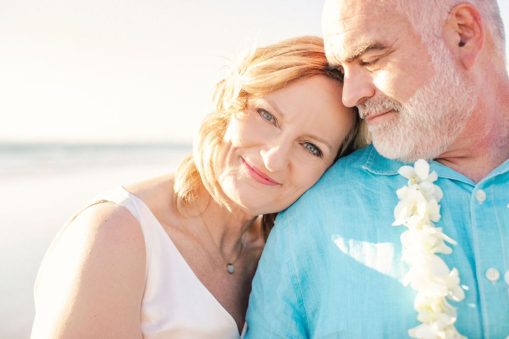An intimate beach portrait of a couple in white clothing with a warm sunset glow.