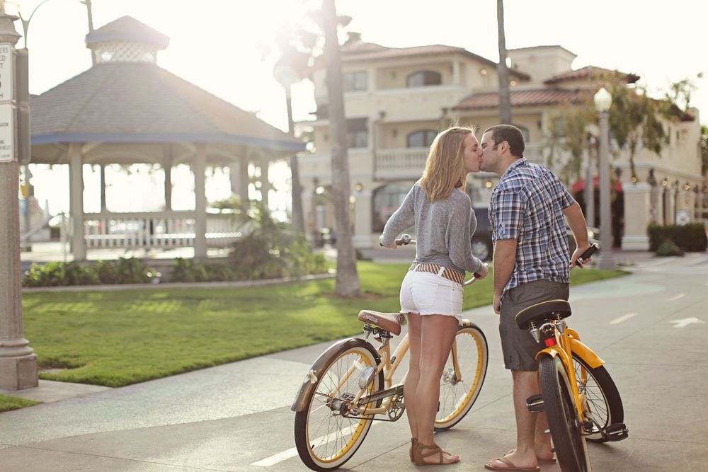 A couple sharing a tender moment with bicycles at sunset near a beach gazebo.