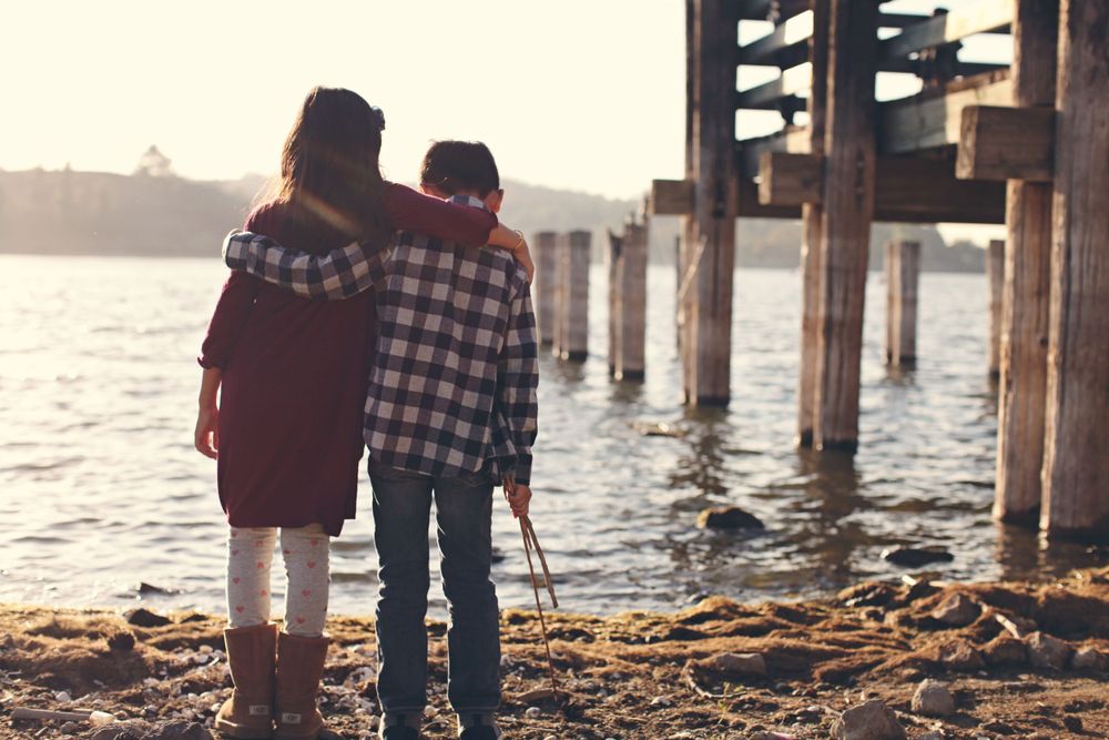 A couple stands close together on a beach at sunset near wooden pier posts.