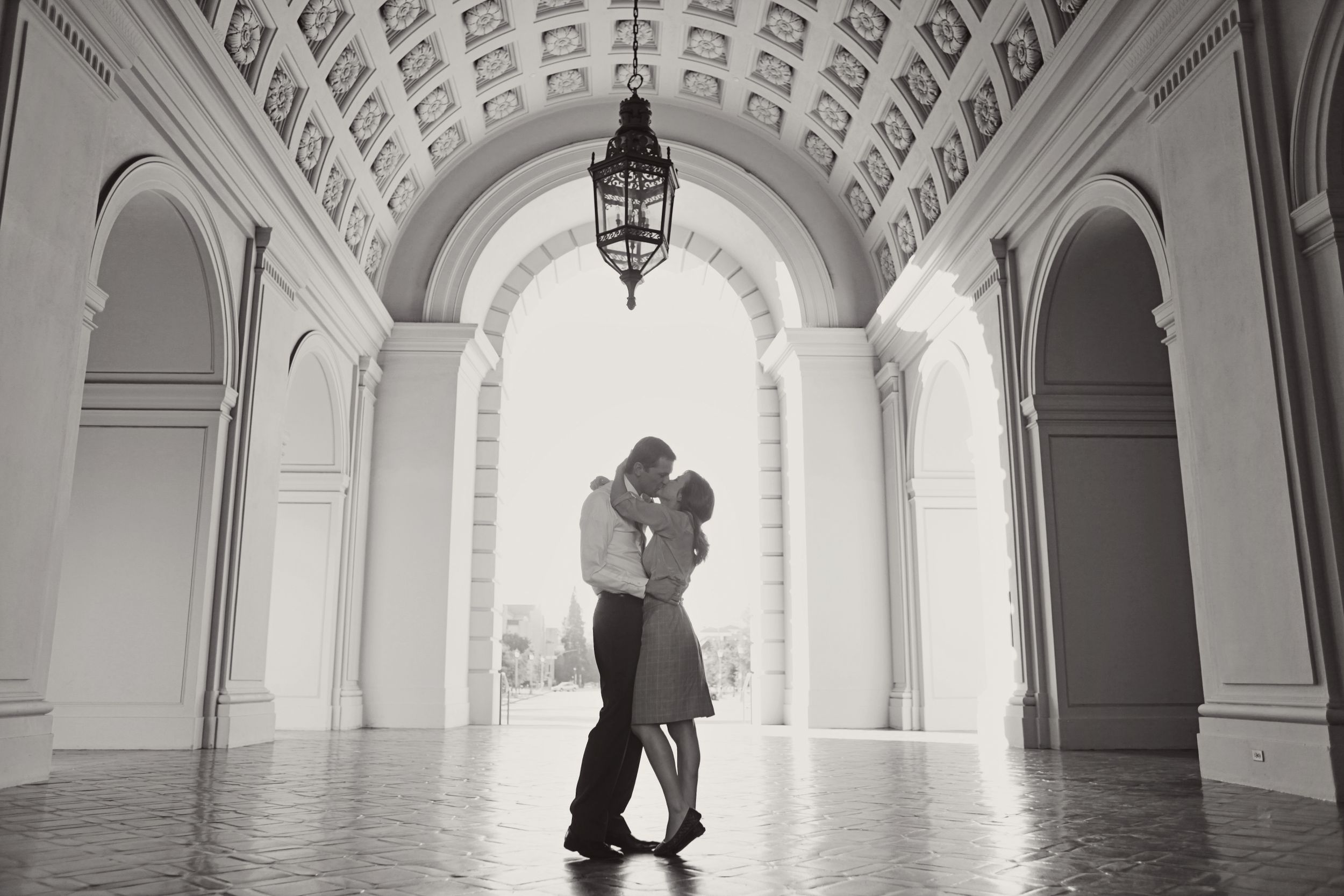 Romantic silhouette of couple embracing under grand architectural archway.