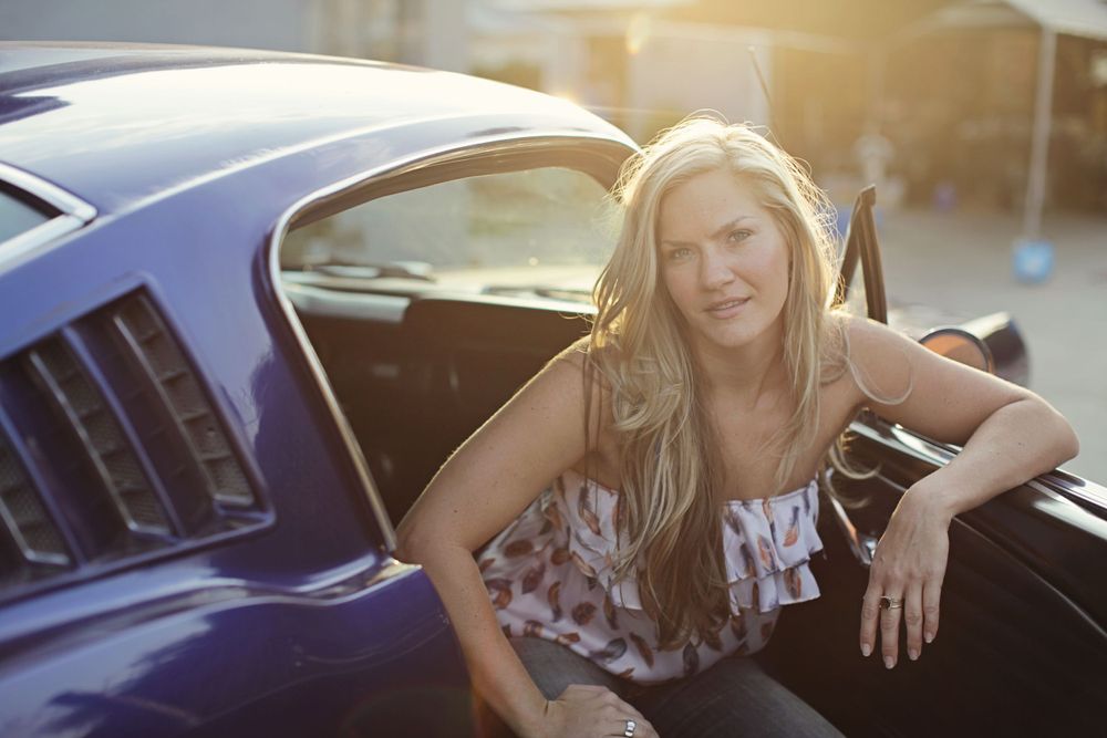 Bright sunlit shot of someone posing against a blue sports car.
