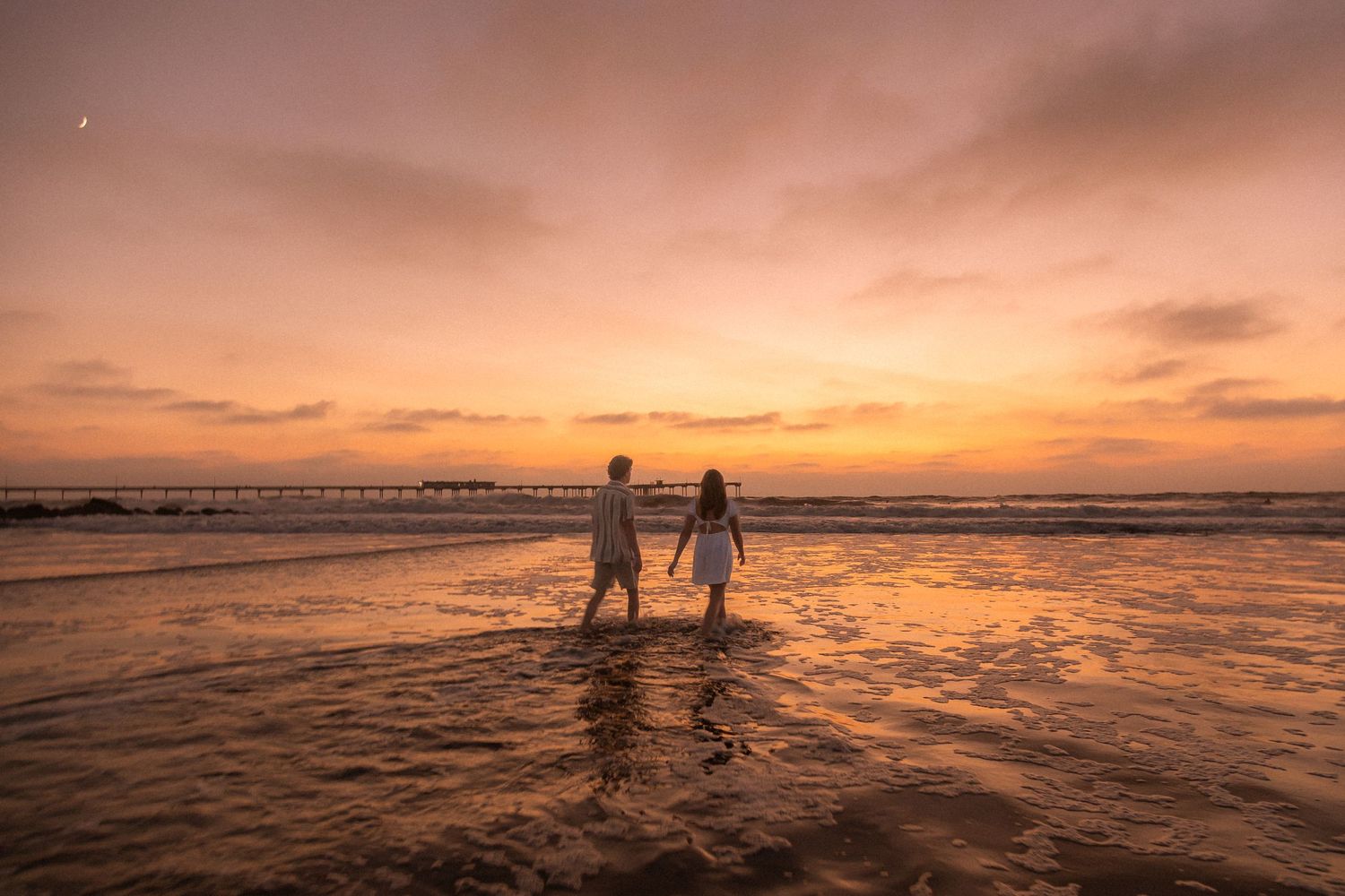 Silhouettes of two figures wading in ocean water during a vibrant sunset.
