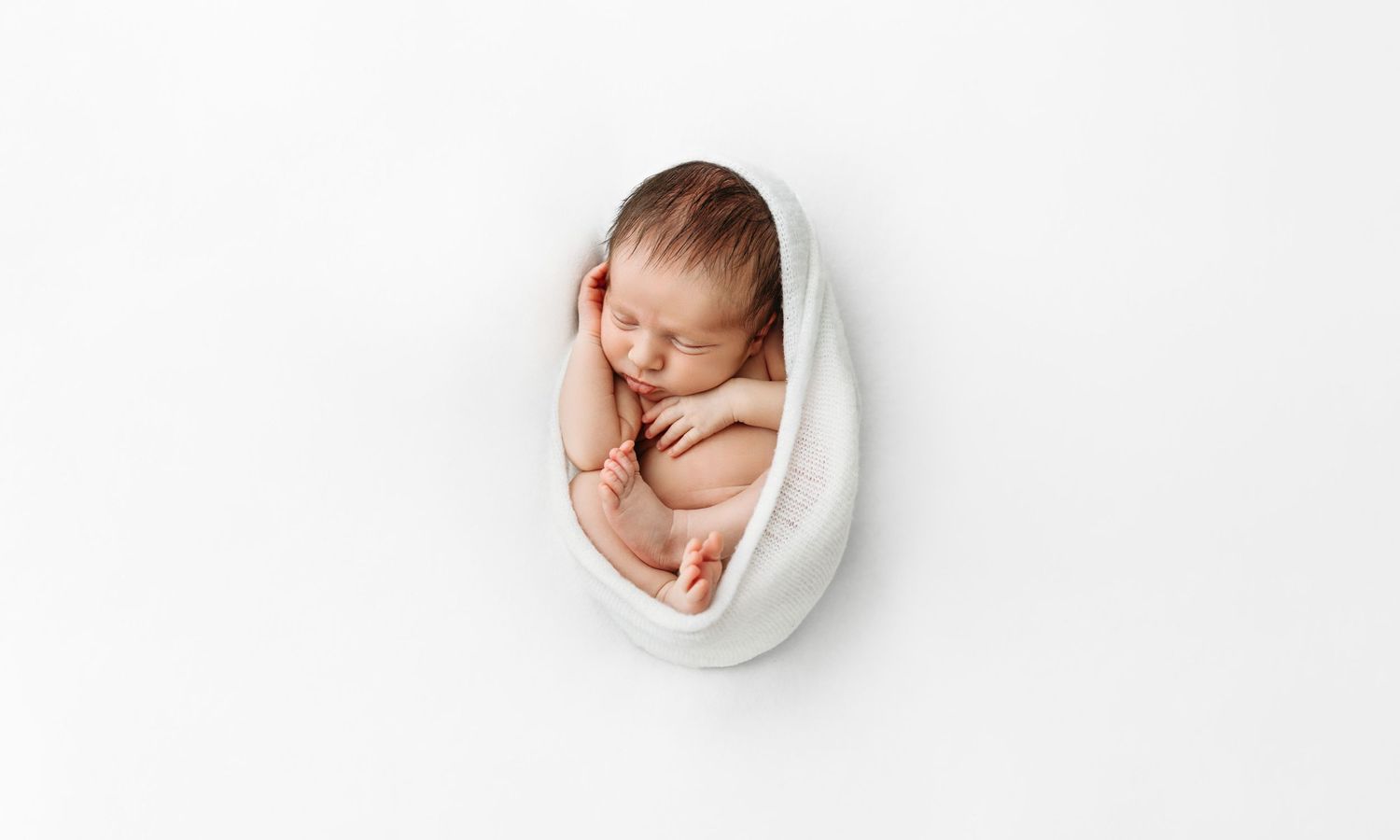 Newborn baby curled up in womb-like wrap