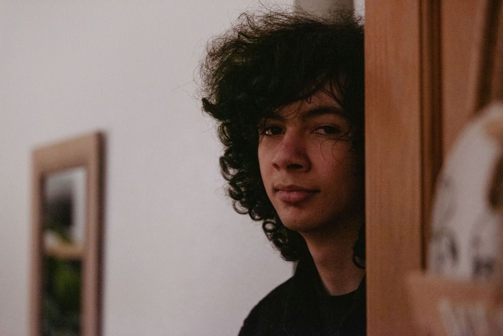 Portrait of a teenage boy with curly hair peeking from behind a doorway