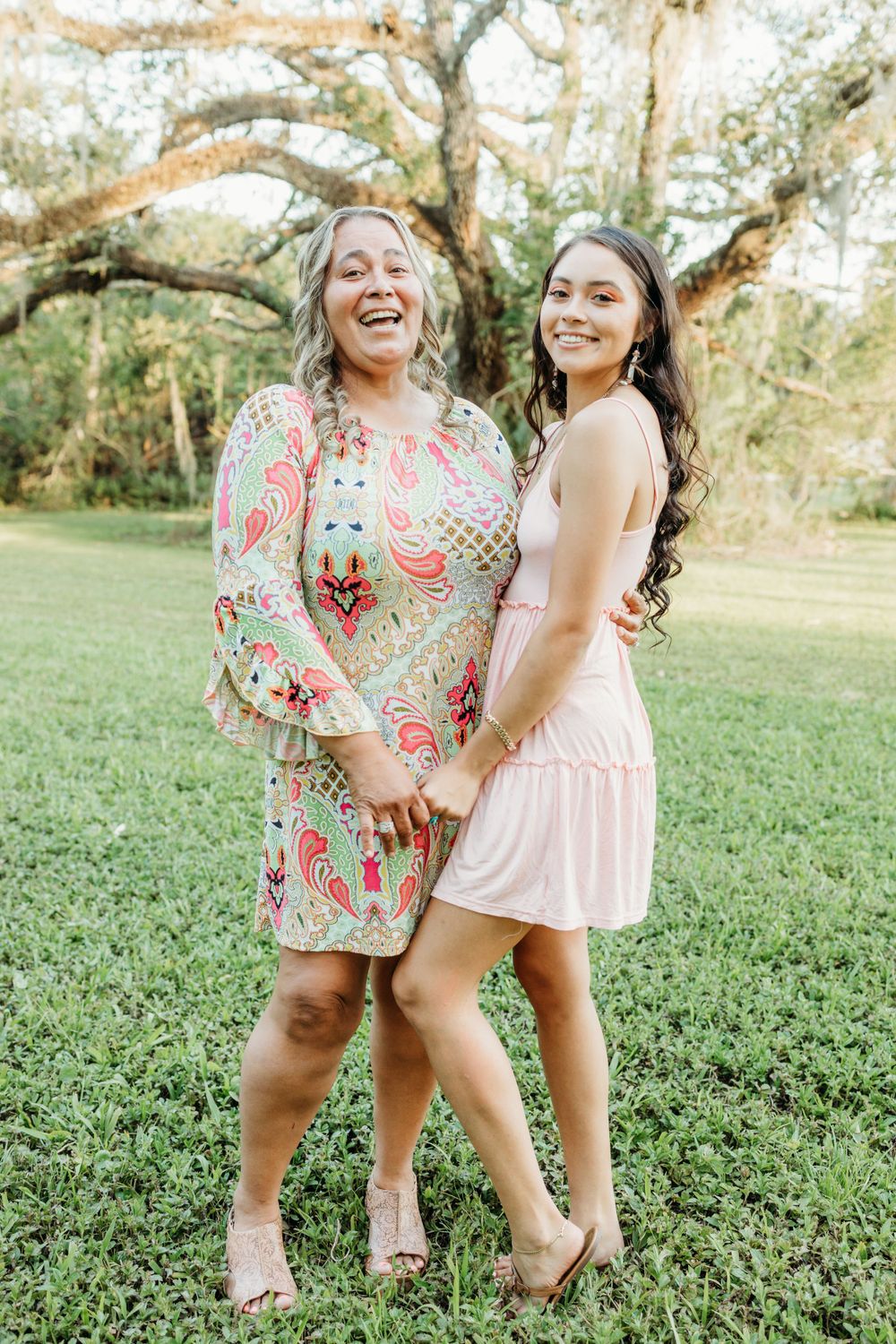 Two women share joyful laughter in a garden setting wearing pink and patterned dresses.