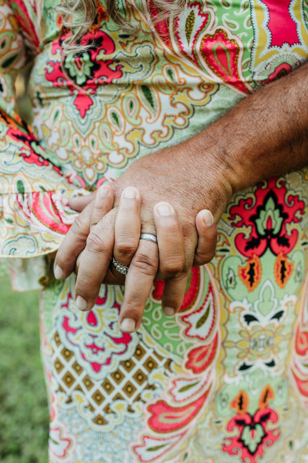 Close-up of hands with rings against colorful floral patterned fabric.