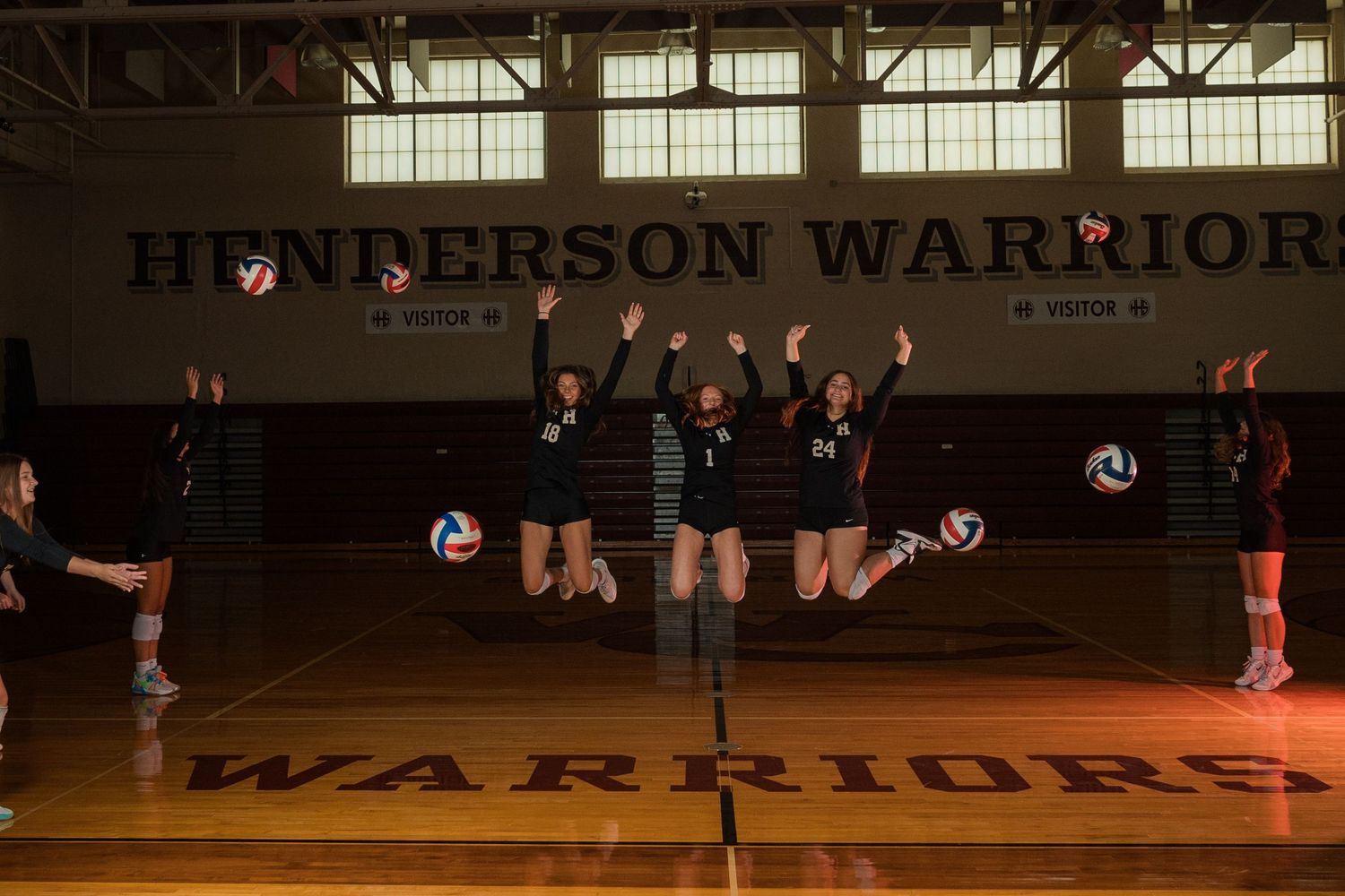 High school volleyball players jumping in unison during practice in a gymnasium.