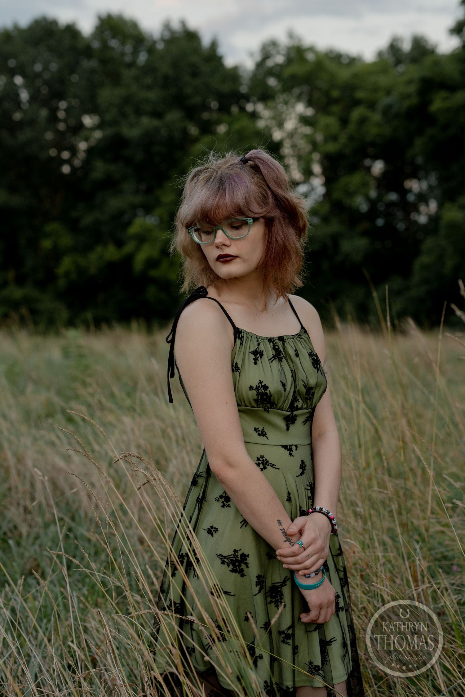 Portrait in a green floral dress standing in tall grass during golden hour.