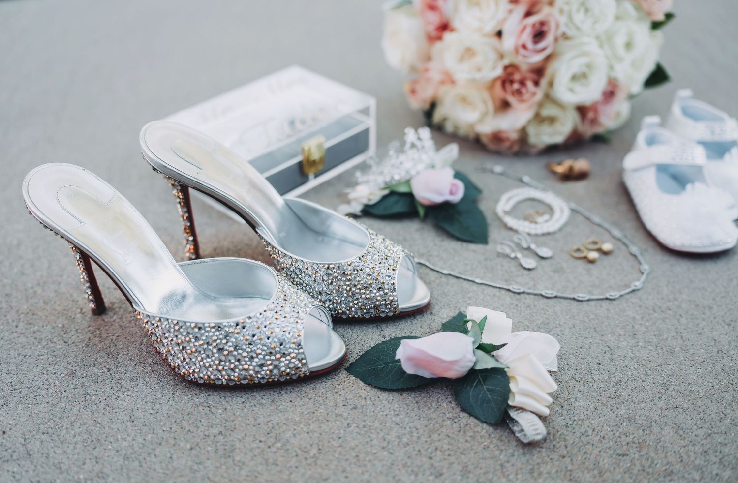 Wedding accessories including sparkly heels, jewelry and pink roses on grey background.