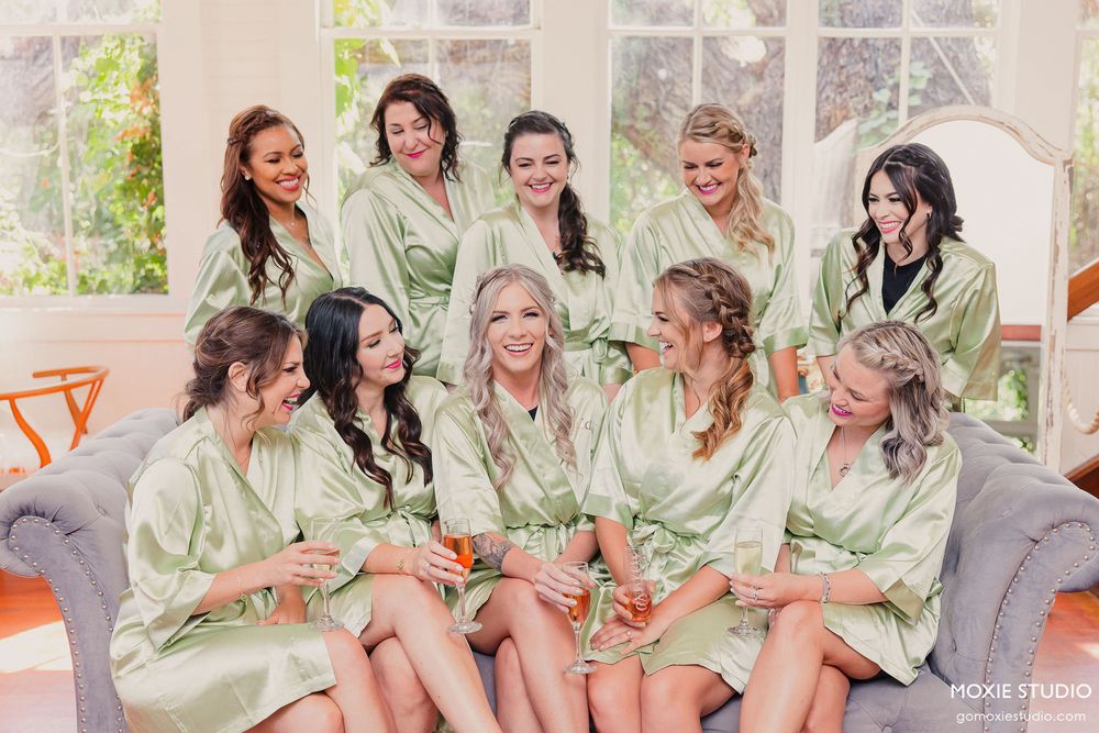 Bridesmaids in matching mint green robes share laughter and joy during pre-wedding preparations.