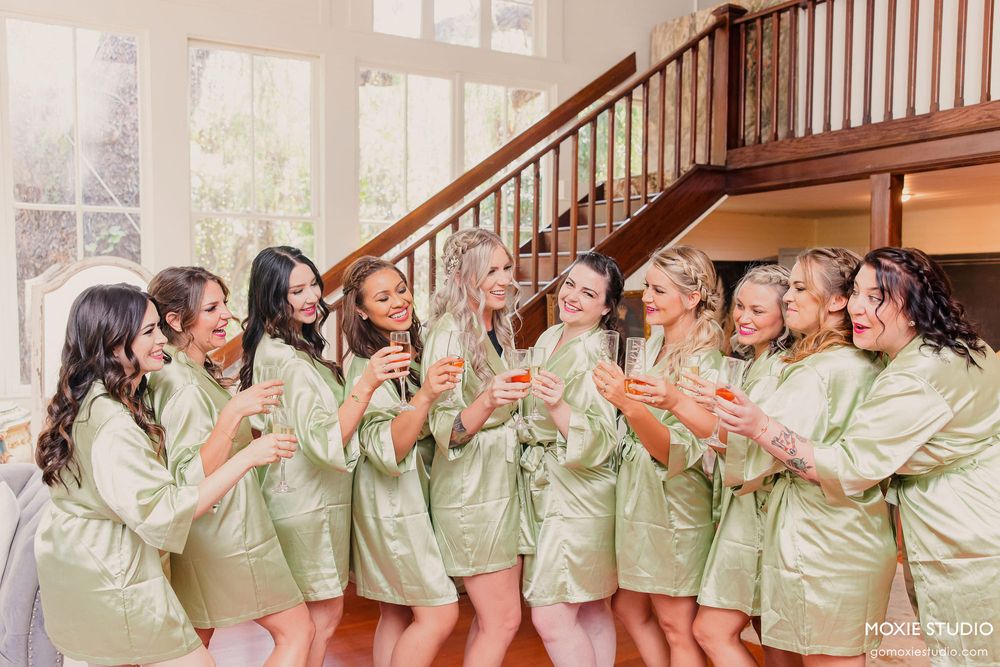 Row of bridesmaids in matching sage robes pose along a wooden staircase.