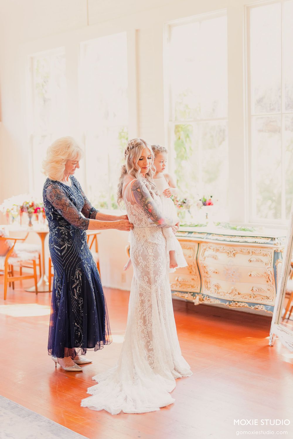Elegant wedding dress being fitted in a bright sunlit room with orange accents.