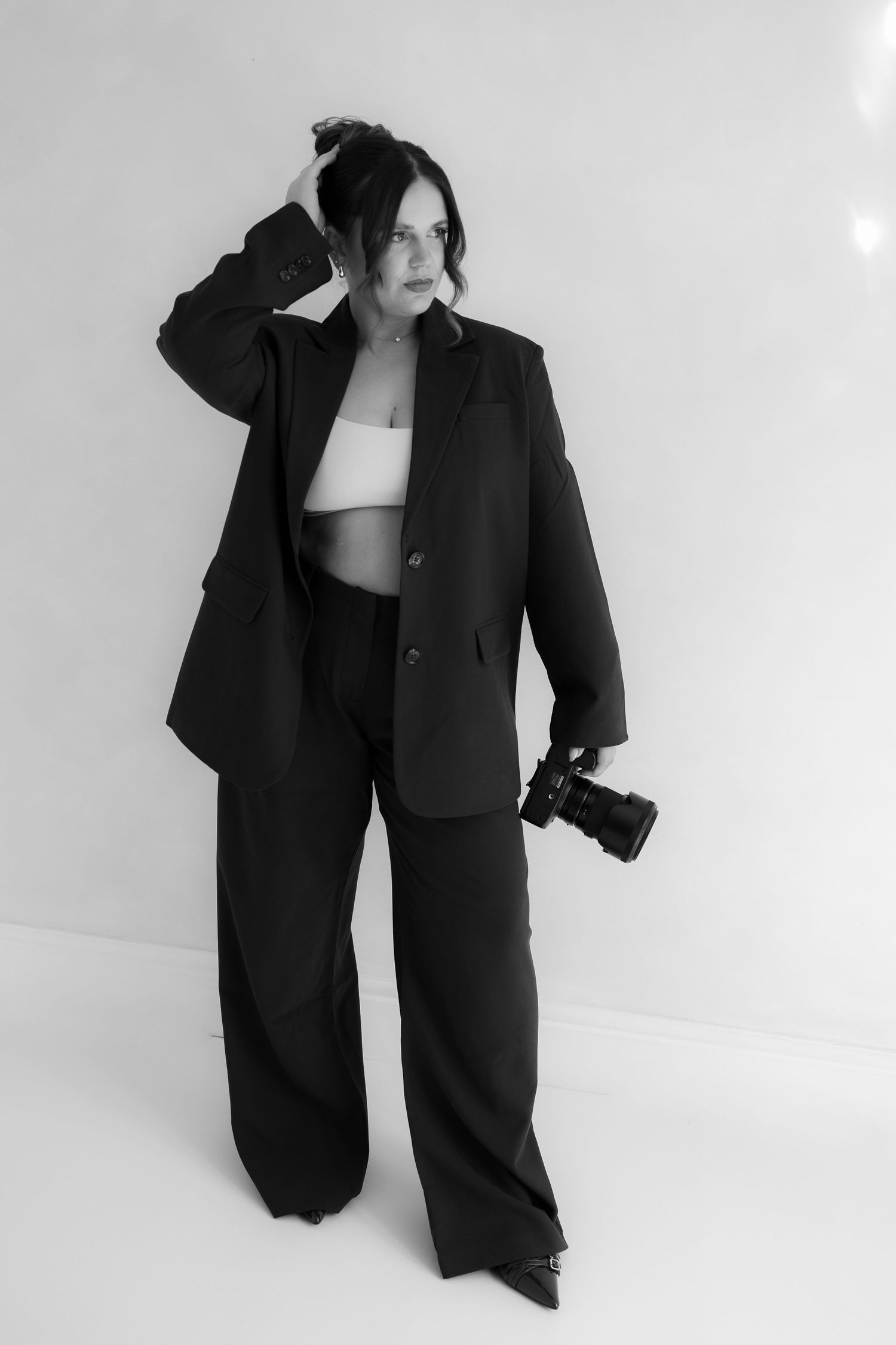 black and white image of photographer branding session while standing in suit holding her camera.