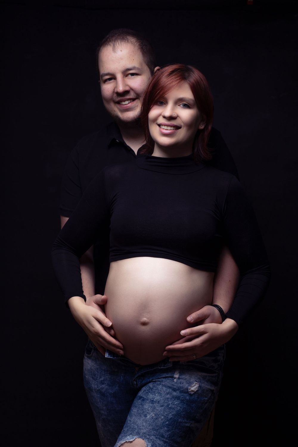 Happy couple smiling together, with the man embracing his pregnant partner and holding her bare baby bump.