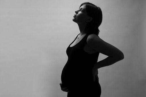 Black and white silhouette of a pregnant woman holding her belly, profile view against a light background.