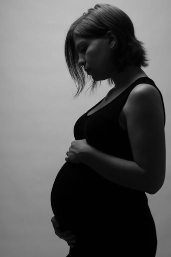 Black and white silhouette of a pregnant woman in a black dress tenderly holding her baby bump.