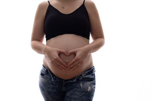 Pregnant woman in black crop top and jeans making a heart shape with her hands on her baby bump.
