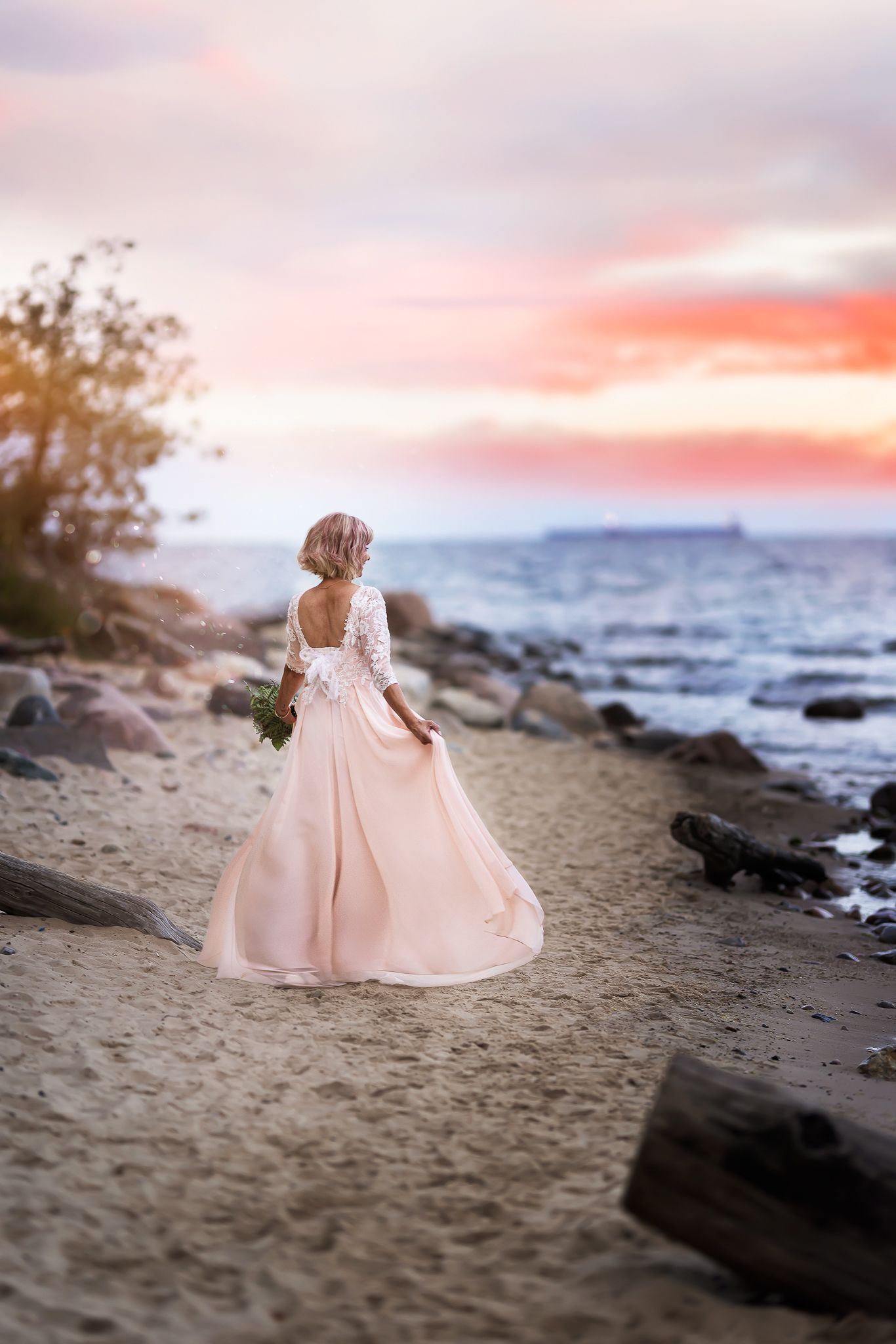 Pink dress flowing in the breeze during a sunset beach photoshoot with rocky coastline.
