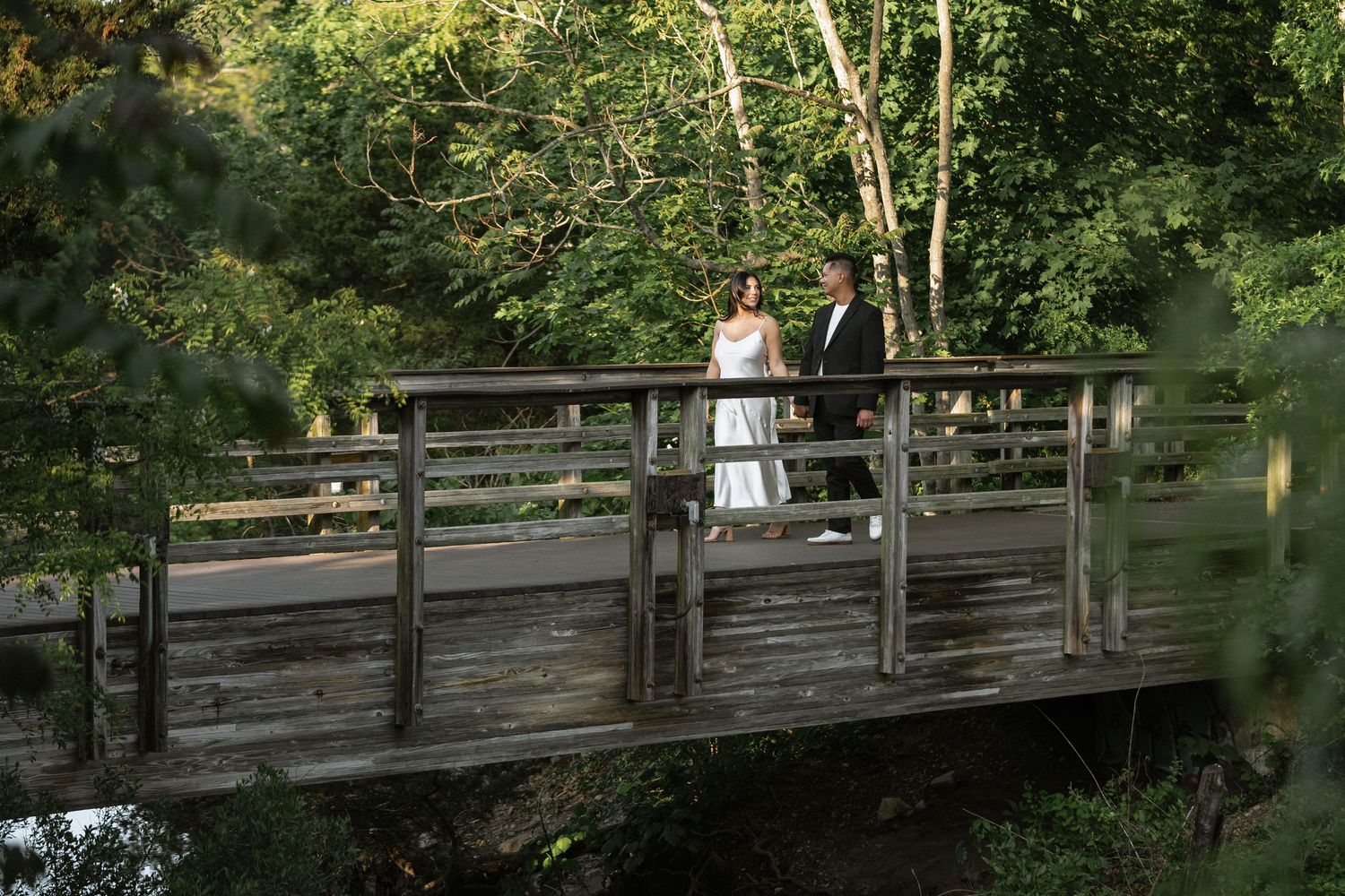 Long wooden bridge pathway through lush green forest scenery.