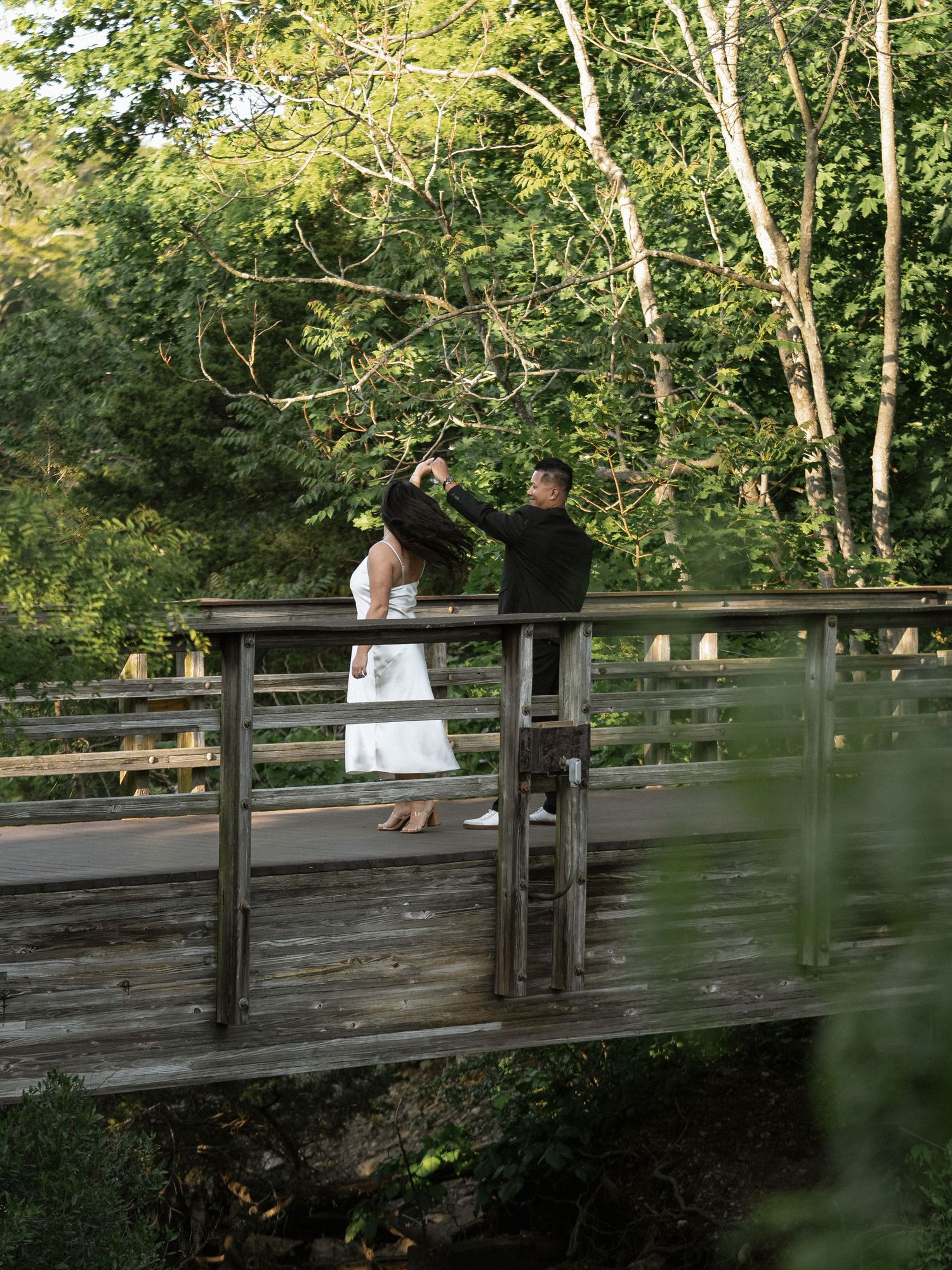 Couple sitting on wooden bridge surrounded by green summer foliage.
