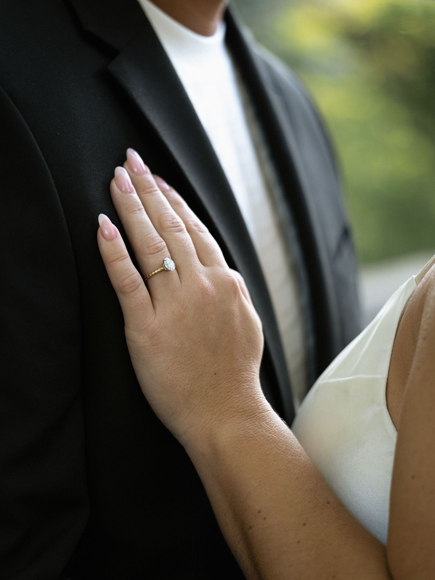 Close-up of engagement ring displayed on hand resting against formal attire.