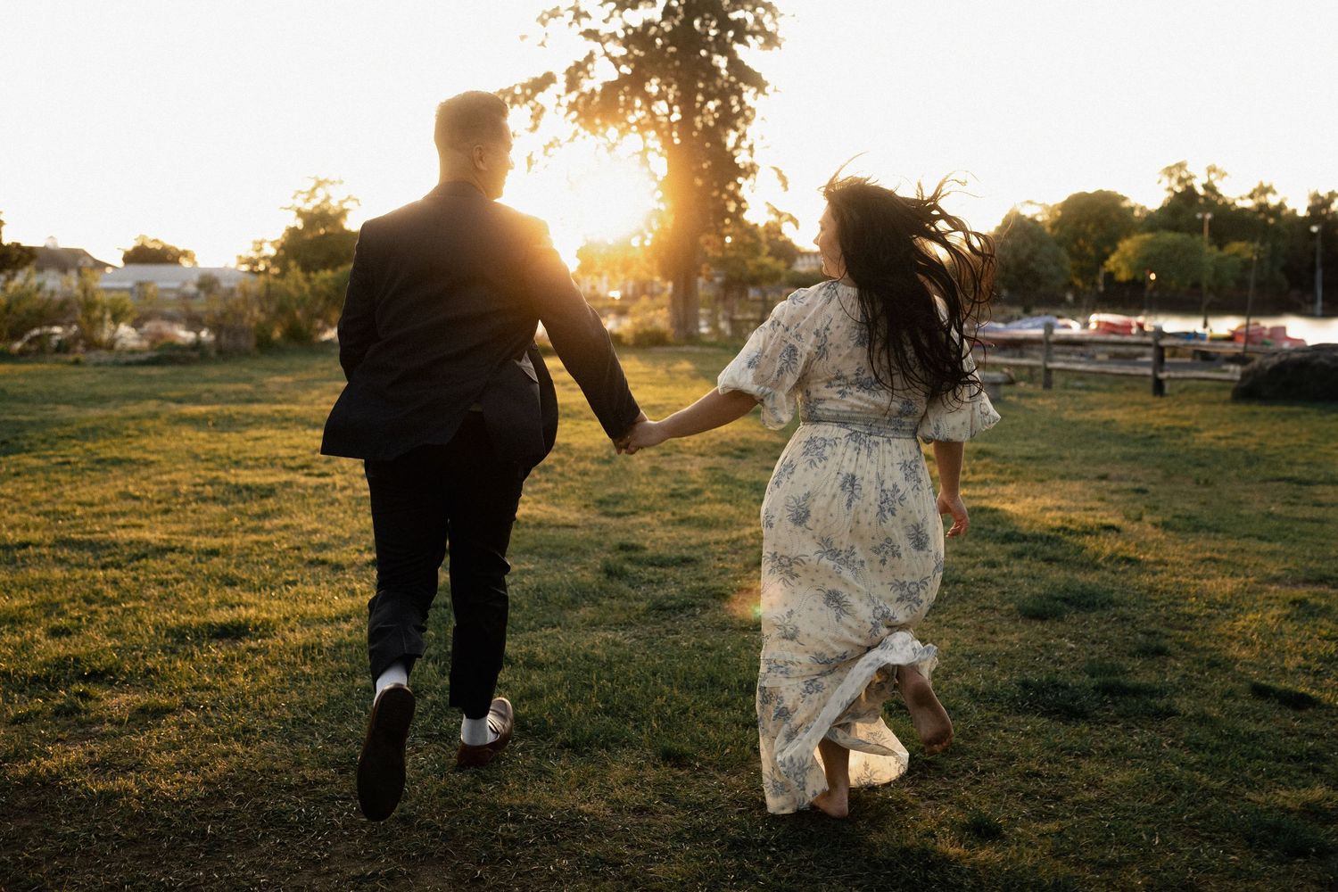 Silhouetted couple running together through grass at sunset.