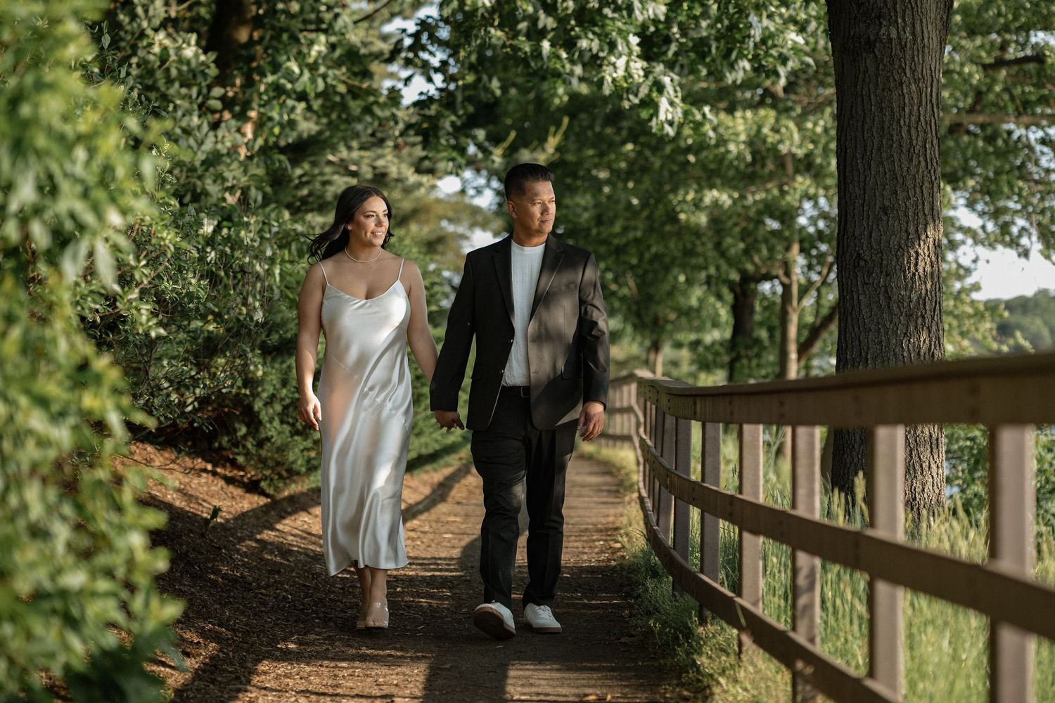 Two people walking along a wooded path during golden hour at a park.