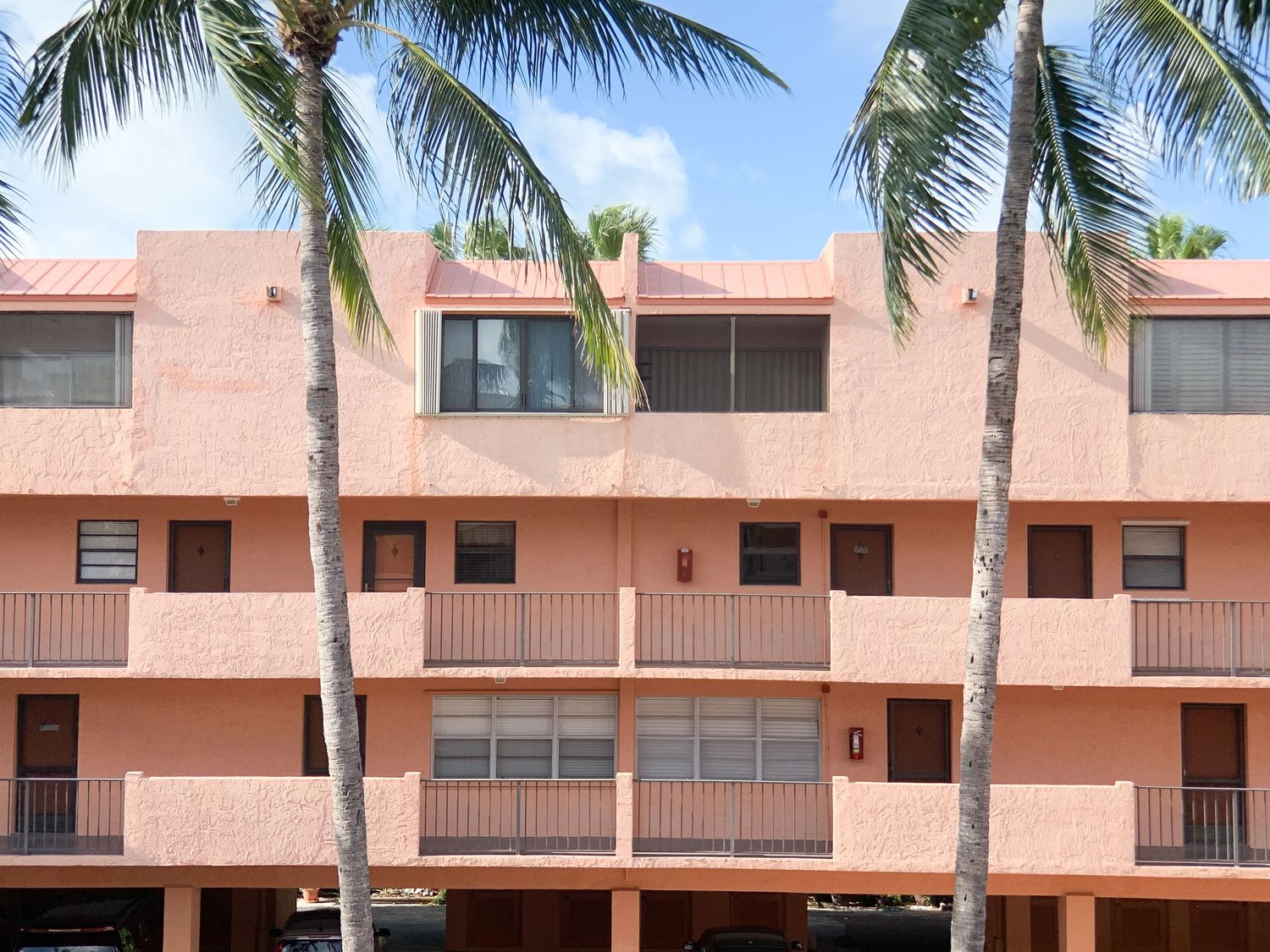 Exterior view of pink condominiums with palm trees along a waterfront.