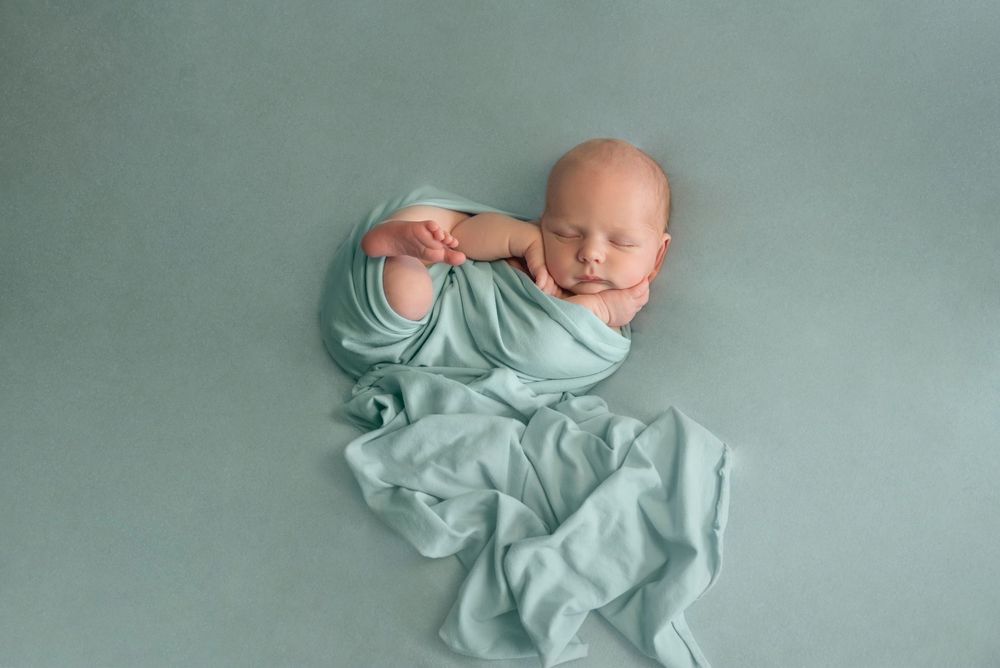 Newborn boy posed sleeping on a green back drop during an in-home newborn session in his own home. Re and calm Bump Birth and Beyond.